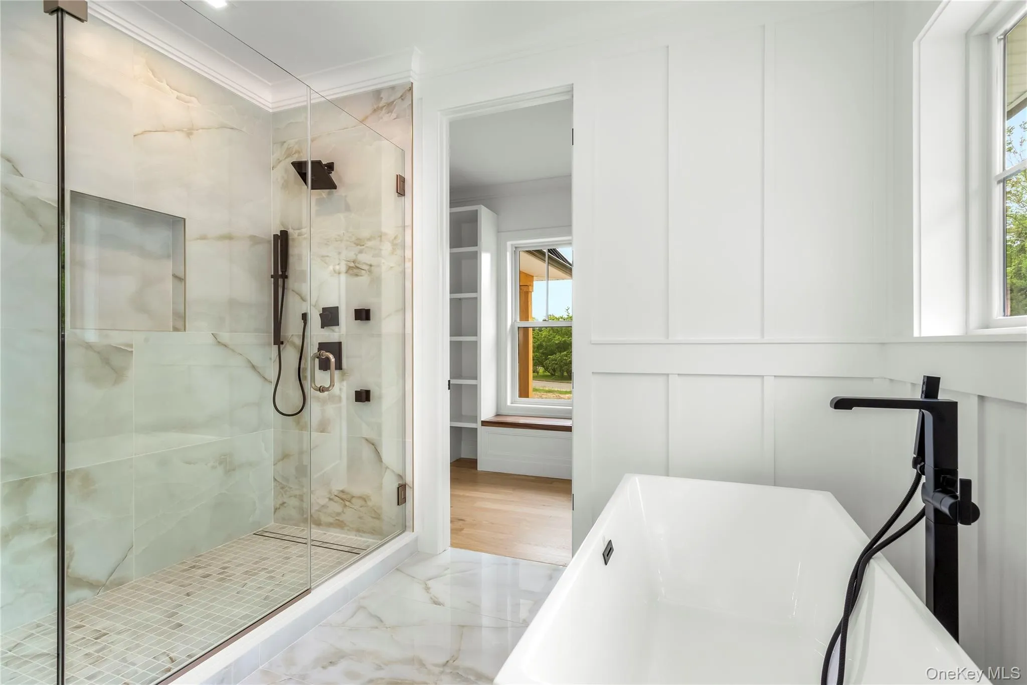 Full bathroom with marble finish flooring, crown molding, a soaking tub, a stall shower, and a decorative wall Full bathroom with marble finish flooring, crown molding, a soaking tub, a stall shower, and a decorative wall