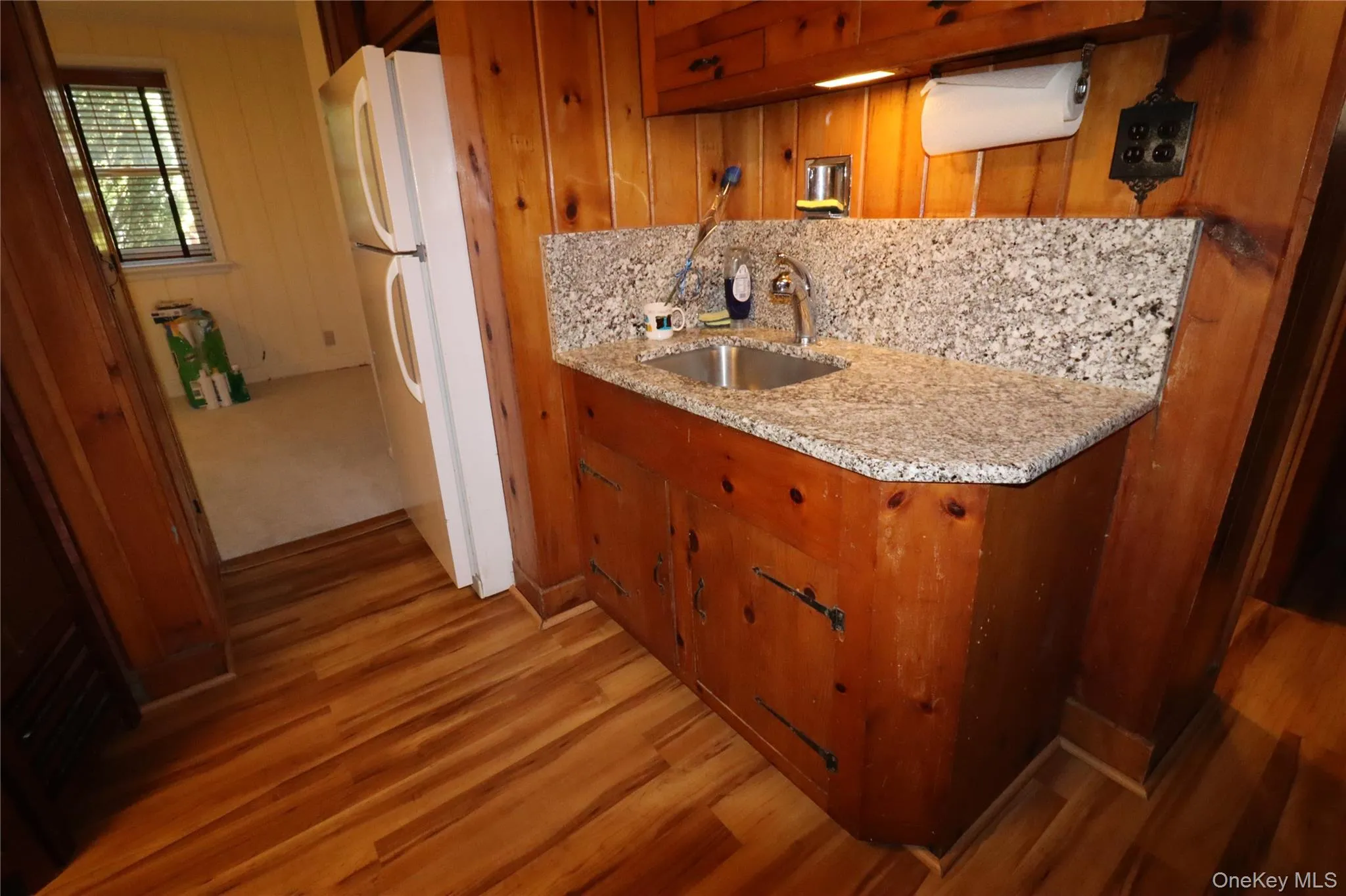 Kitchen with light wood finished floors, brown cabinets, a sink, freestanding refrigerator, and wooden walls Kitchen with light wood finished floors, brown cabinets, a sink, freestanding refrigerator, and wooden walls
