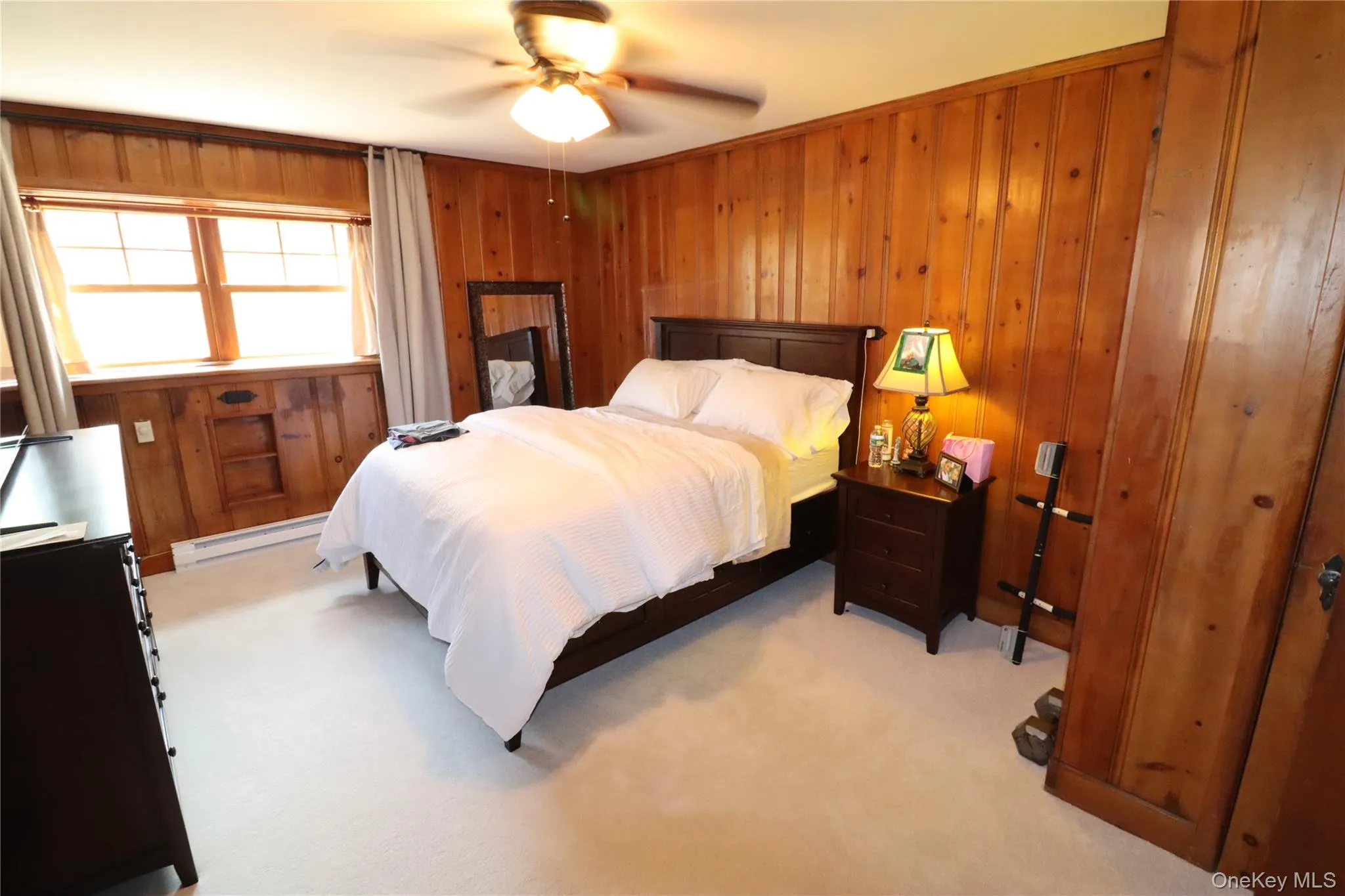 Bedroom featuring a baseboard radiator, light carpet, ceiling fan, and wood walls Bedroom featuring a baseboard radiator, light carpet, ceiling fan, and wood walls