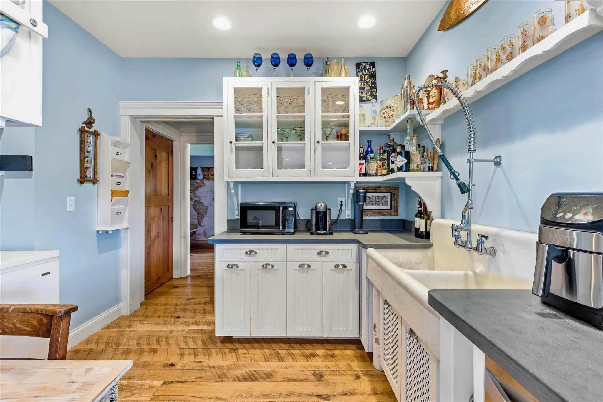 Kitchen with light wood finished floors, black microwave, white cabinetry, and glass insert cabinets Kitchen with light wood finished floors, black microwave, white cabinetry, and glass insert cabinets