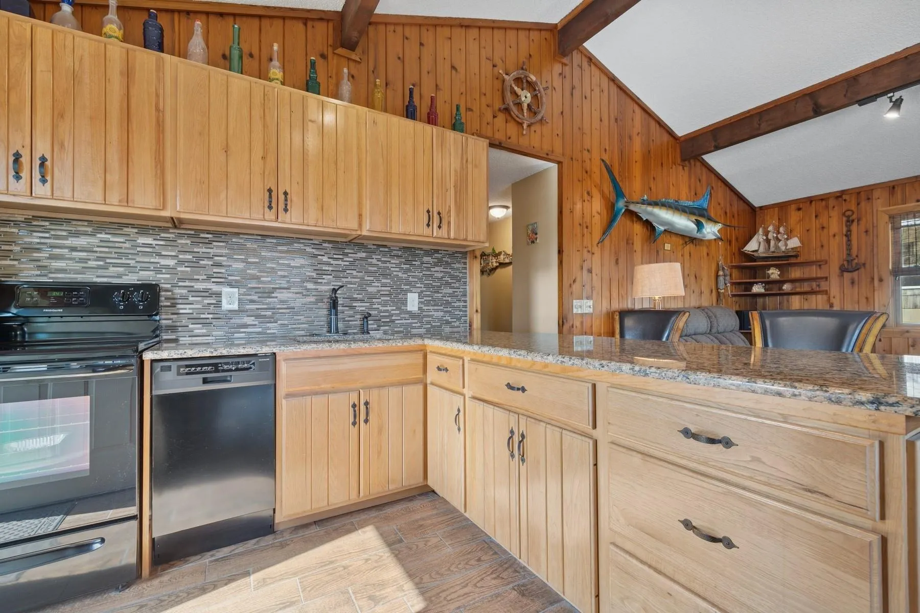 Kitchen with tasteful backsplash, wood walls, a sink, dishwashing machine, and black range with electric cooktop Kitchen with tasteful backsplash, wood walls, a sink, dishwashing machine, and black range with electric cooktop