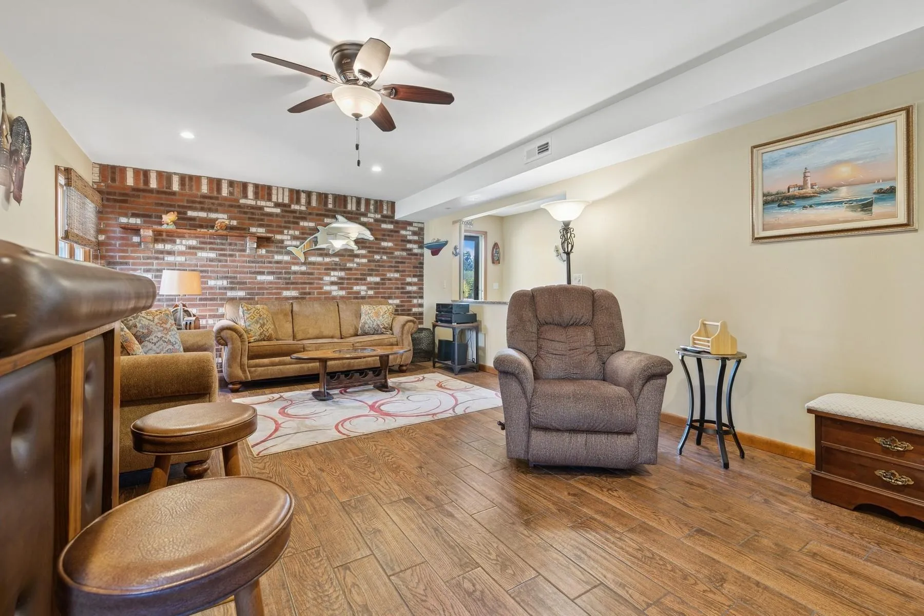 Living area featuring a ceiling fan, brick wall, visible vents, wood finished floors, and baseboards Living area featuring a ceiling fan, brick wall, visible vents, wood finished floors, and baseboards