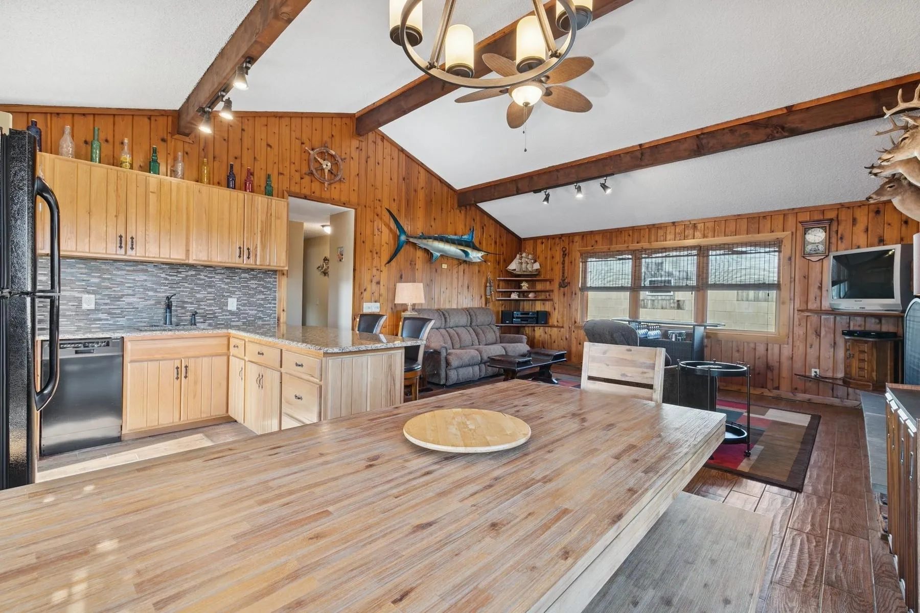 Dining space featuring rail lighting, wood walls, a ceiling fan, vaulted ceiling with beams, and light wood-type flooring Dining space featuring rail lighting, wood walls, a ceiling fan, vaulted ceiling with beams, and light wood-type flooring