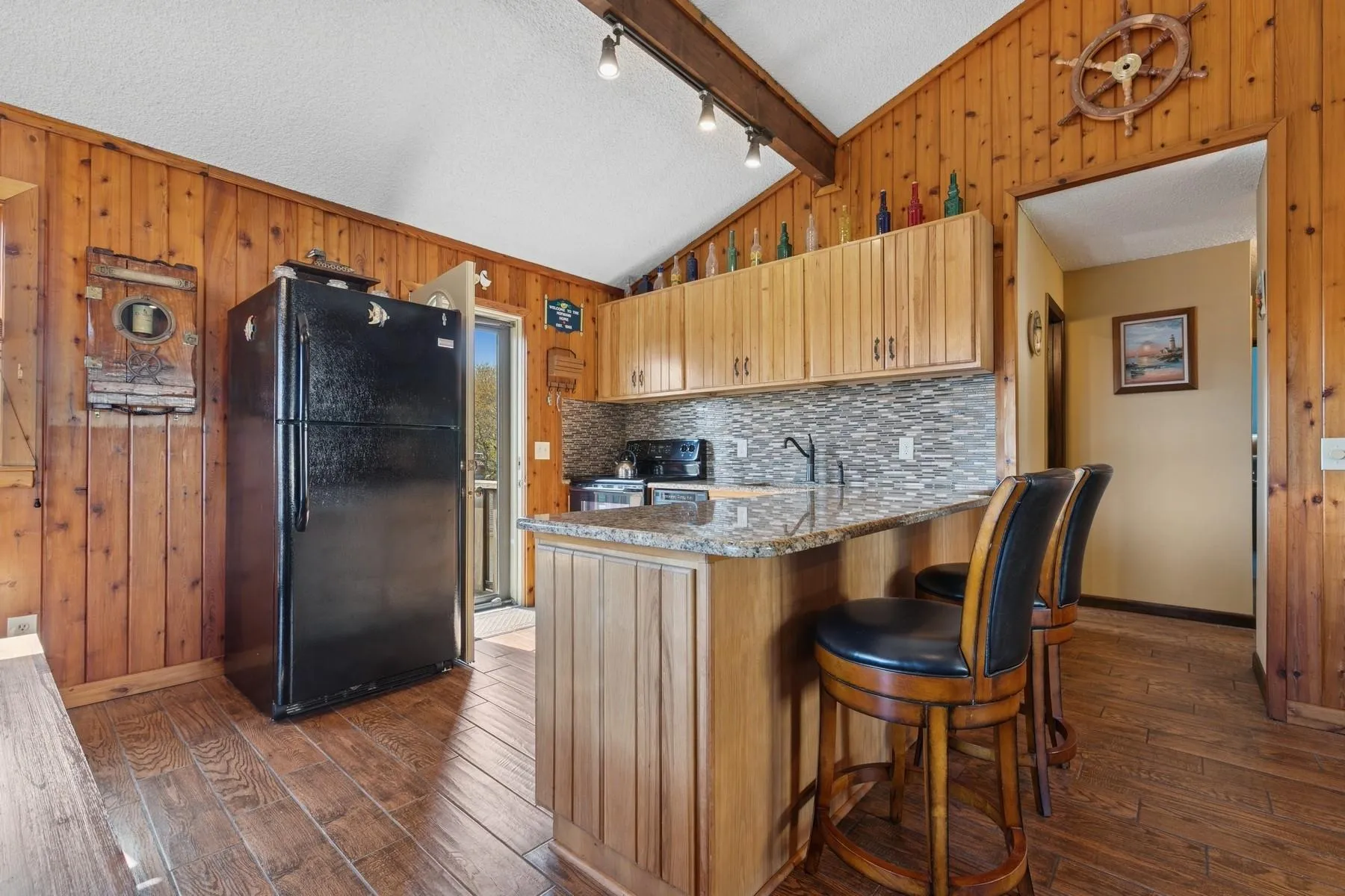 Kitchen with freestanding refrigerator, wood walls, baseboards, dark wood-type flooring, and vaulted ceiling Kitchen with freestanding refrigerator, wood walls, baseboards, dark wood-type flooring, and vaulted ceiling