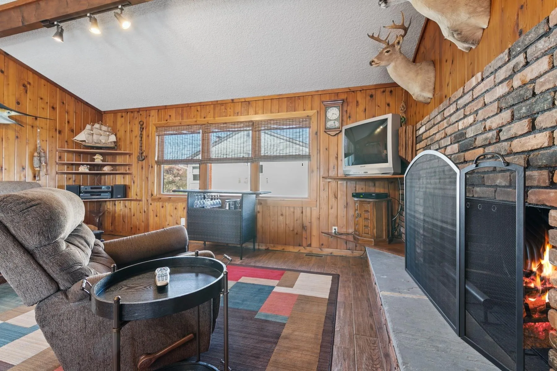 Living room with wooden walls, rail lighting, a warm lit fireplace, and hardwood / wood-style floors Living room with wooden walls, rail lighting, a warm lit fireplace, and hardwood / wood-style floors