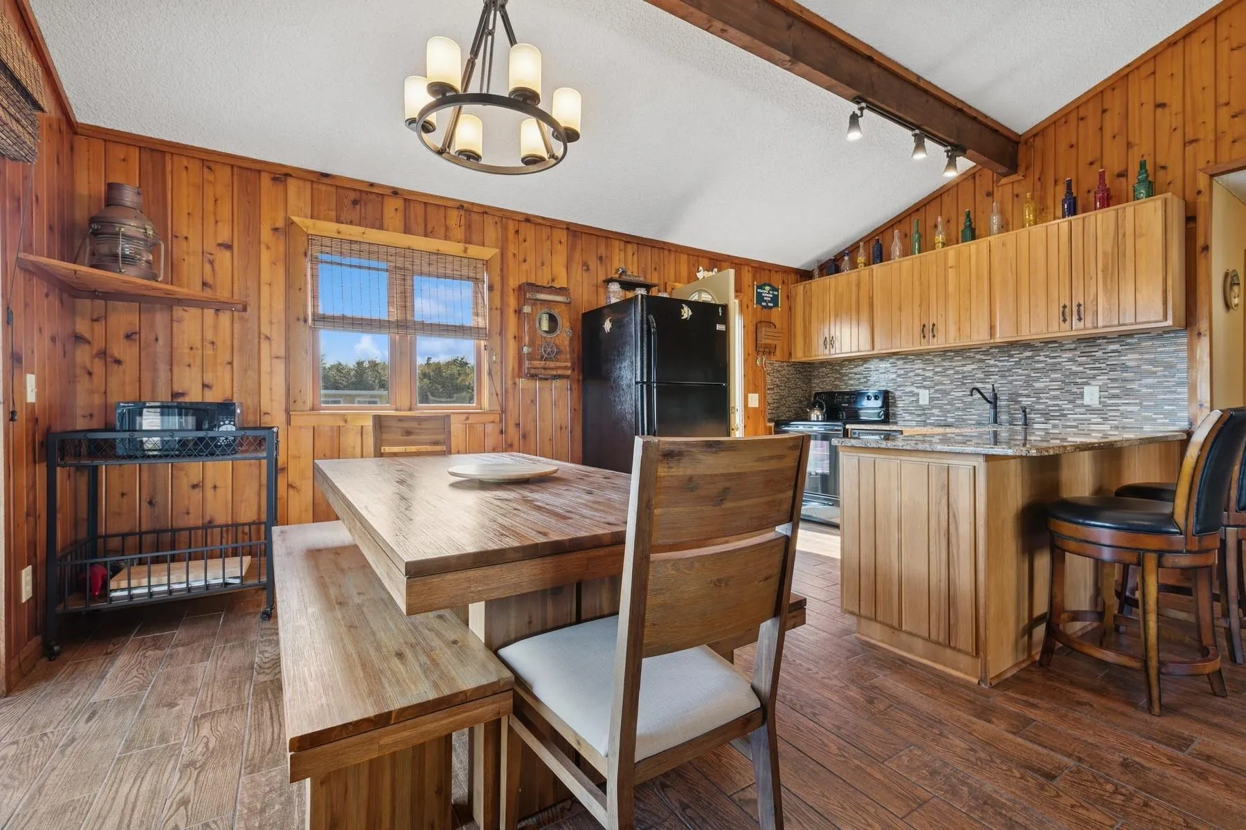 Kitchen featuring wooden walls, a notable chandelier, lofted ceiling with beams, freestanding refrigerator, and dark wood-type flooring Kitchen featuring wooden walls, a notable chandelier, lofted ceiling with beams, freestanding refrigerator, and dark wood-type flooring