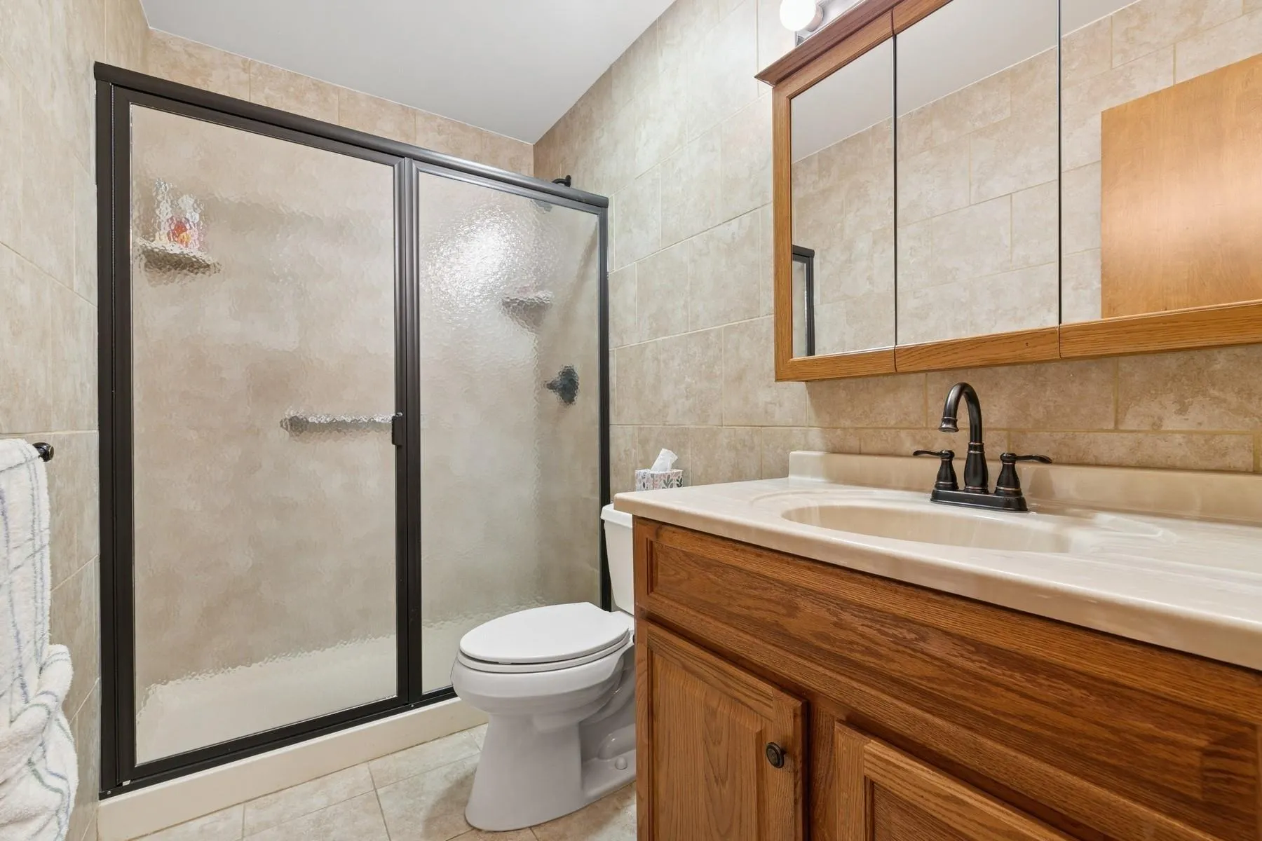 Bathroom featuring tile patterned flooring, vanity, toilet, tile walls, and a stall shower Bathroom featuring tile patterned flooring, vanity, toilet, tile walls, and a stall shower