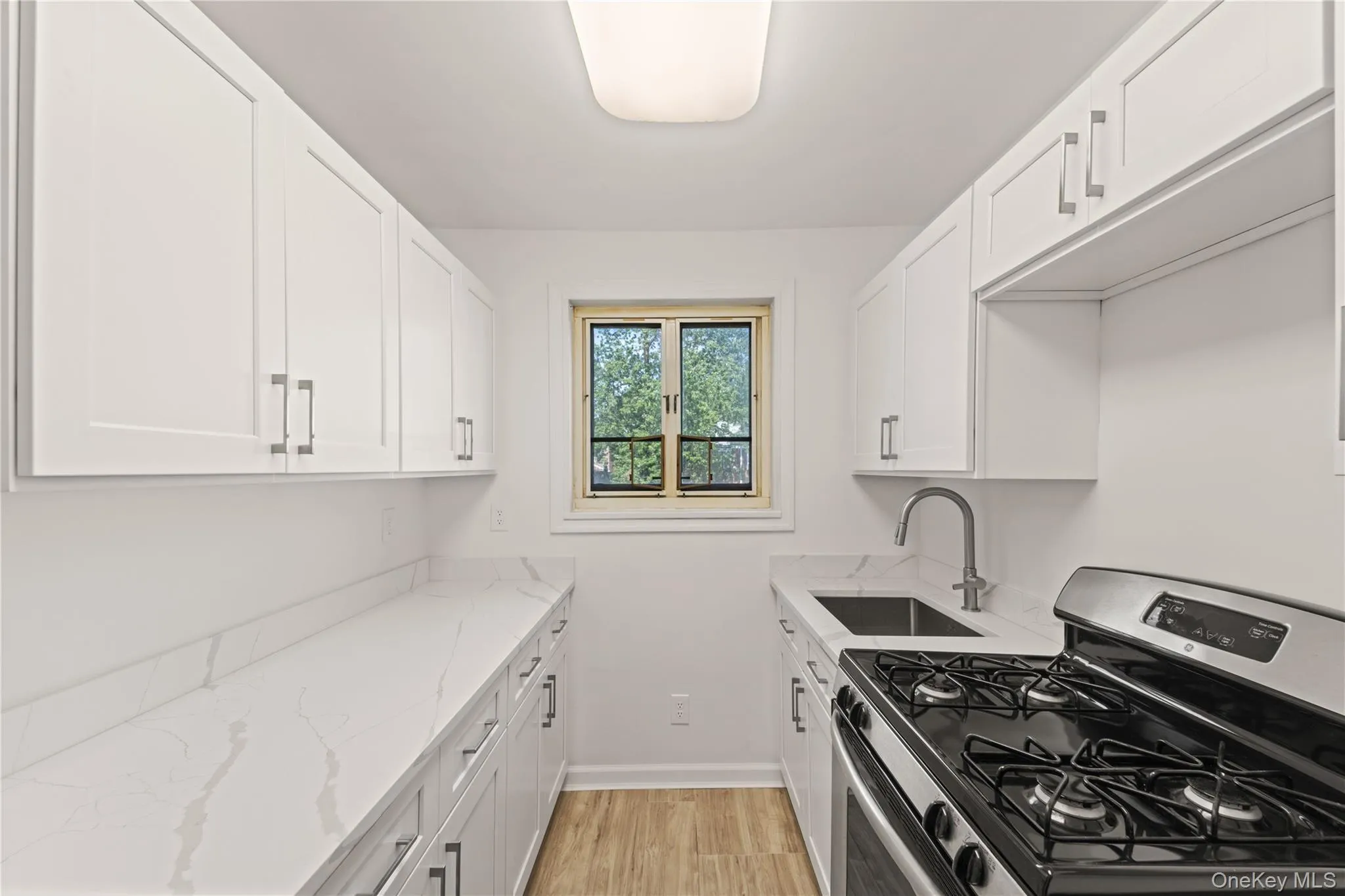 Kitchen with stainless steel range with gas stovetop, light wood-type flooring, white cabinetry, and light stone countertops Kitchen with stainless steel range with gas stovetop, light wood-type flooring, white cabinetry, and light stone countertops