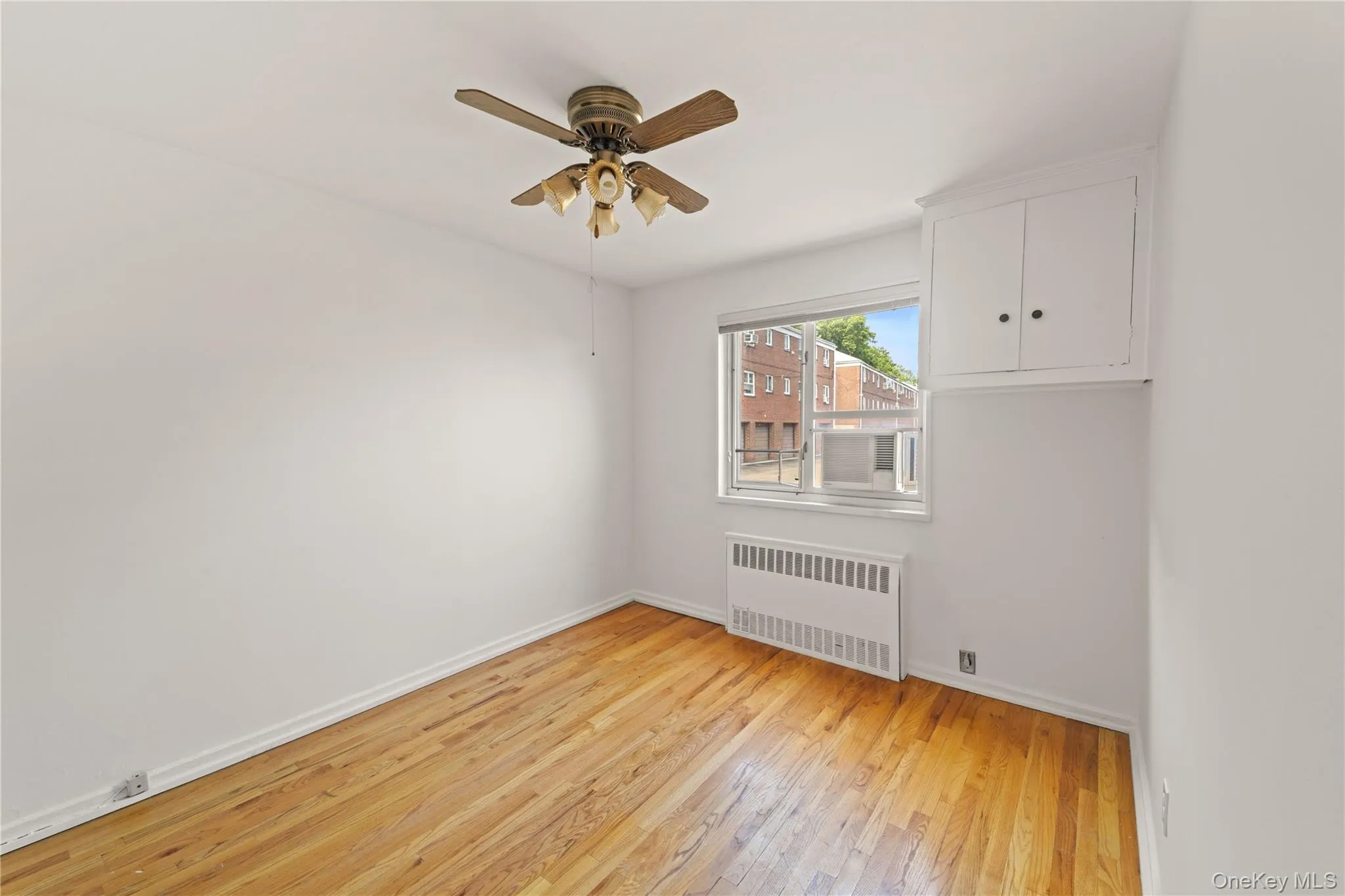 Spare room featuring light wood-style floors, radiator, and a ceiling fan Spare room featuring light wood-style floors, radiator, and a ceiling fan