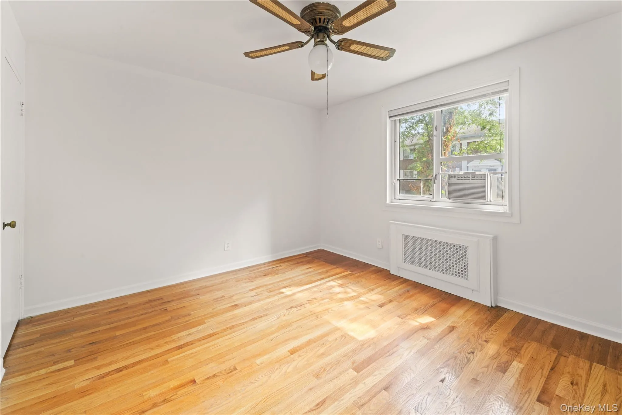 Empty room featuring radiator, light wood-style flooring, ceiling fan, and cooling unit Empty room featuring radiator, light wood-style flooring, ceiling fan, and cooling unit