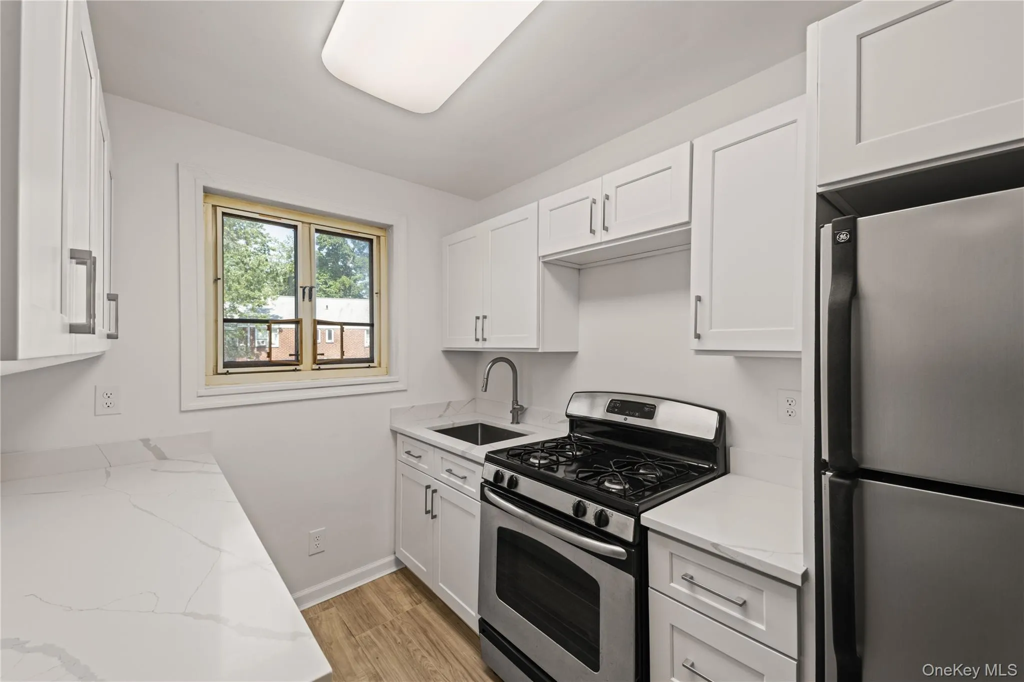 Kitchen with stainless steel appliances, white cabinetry, light wood-type flooring, and light stone countertops Kitchen with stainless steel appliances, white cabinetry, light wood-type flooring, and light stone countertops