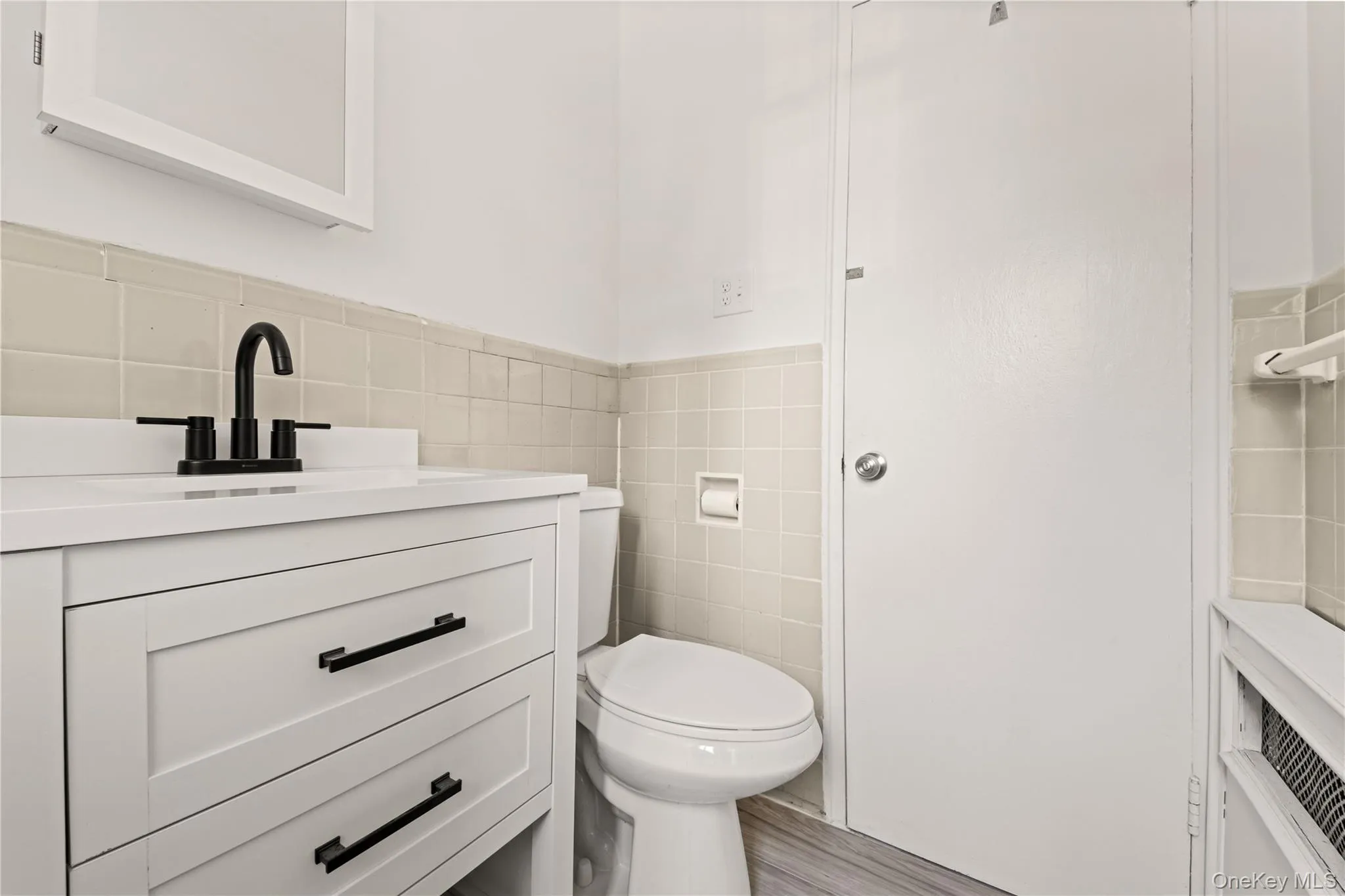 Half bathroom featuring tile walls, a wainscoted wall, vanity, and wood finished floors Half bathroom featuring tile walls, a wainscoted wall, vanity, and wood finished floors