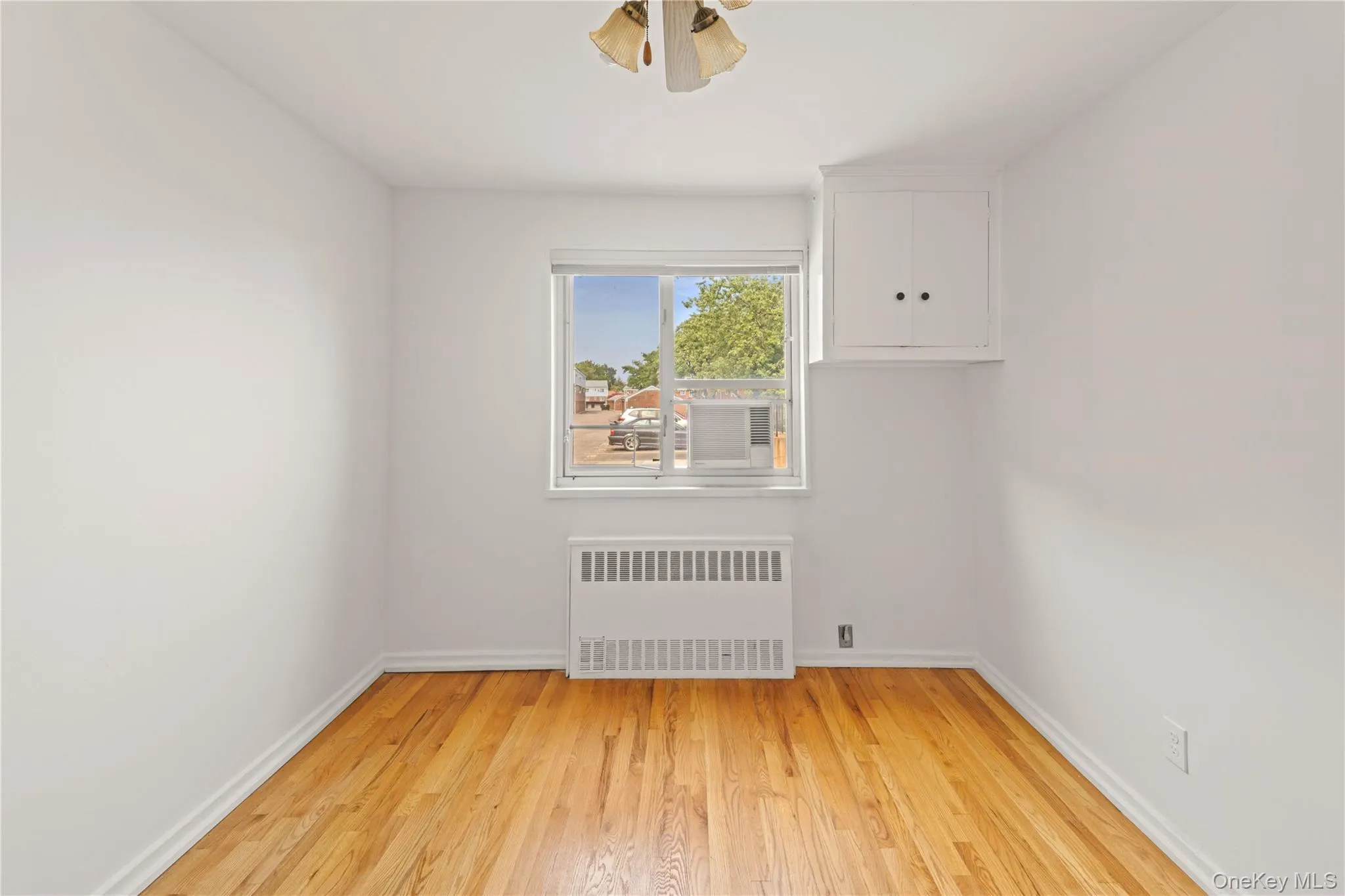 Unfurnished room featuring light wood-style flooring, radiator heating unit, and ceiling fan Unfurnished room featuring light wood-style flooring, radiator heating unit, and ceiling fan