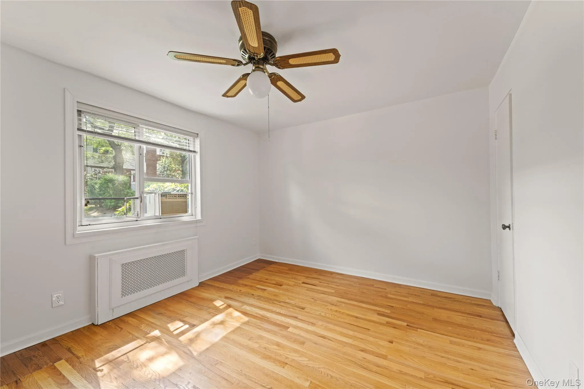 Empty room featuring radiator heating unit, light wood-type flooring, and ceiling fan Empty room featuring radiator heating unit, light wood-type flooring, and ceiling fan