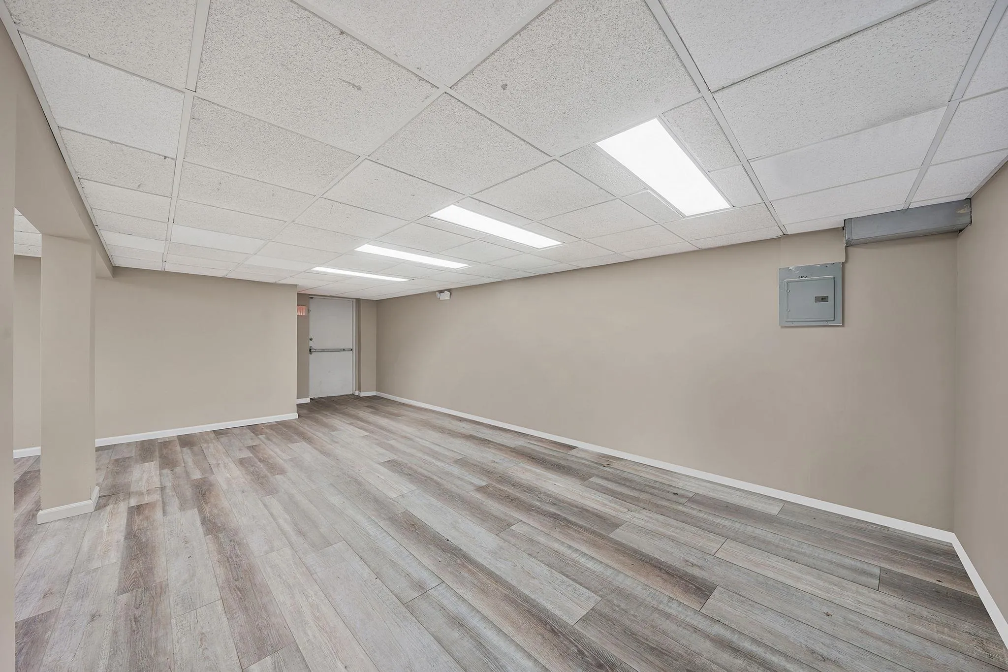 Finished basement with baseboards, a drop ceiling, wood finished floors, and electric panel Finished basement with baseboards, a drop ceiling, wood finished floors, and electric panel