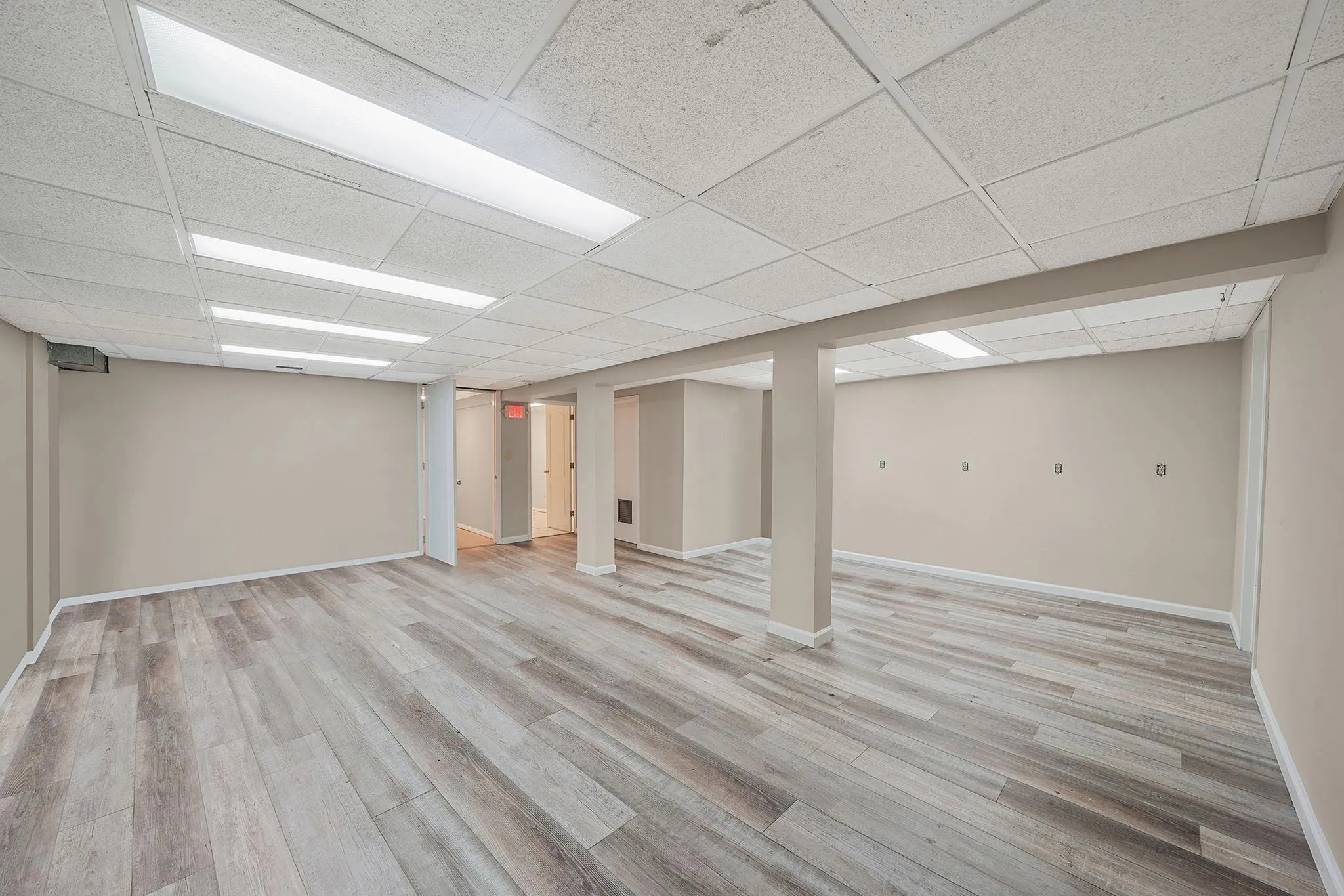 Finished below grade area with baseboards, a drop ceiling, and light wood-style flooring Finished below grade area with baseboards, a drop ceiling, and light wood-style flooring