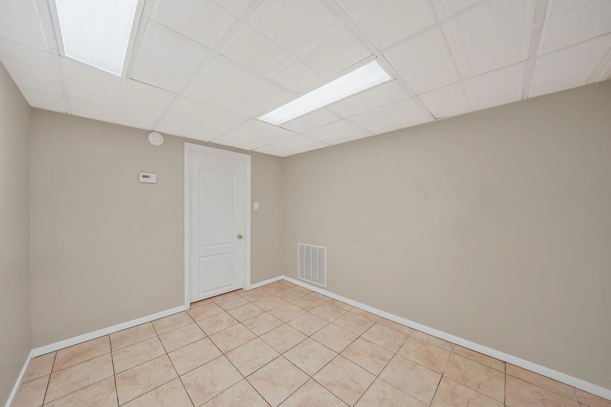 Empty room with light tile patterned flooring, baseboards, visible vents, and a paneled ceiling Empty room with light tile patterned flooring, baseboards, visible vents, and a paneled ceiling