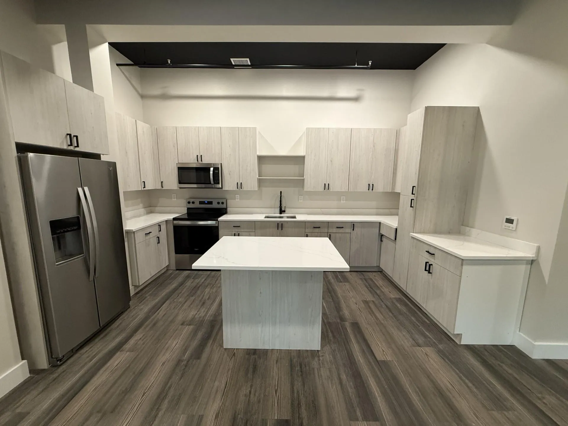 Kitchen featuring appliances with stainless steel finishes, a sink, a center island, open shelves, and dark wood-style flooring Kitchen featuring appliances with stainless steel finishes, a sink, a center island, open shelves, and dark wood-style flooring