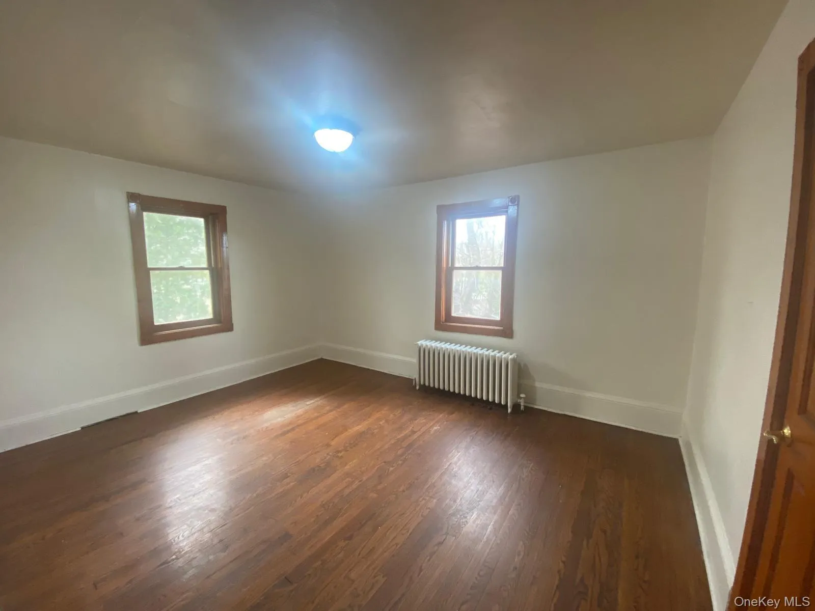 Empty room featuring radiator heating unit, baseboards, dark wood-type flooring, and a healthy amount of sunlight Empty room featuring radiator heating unit, baseboards, dark wood-type flooring, and a healthy amount of sunlight
