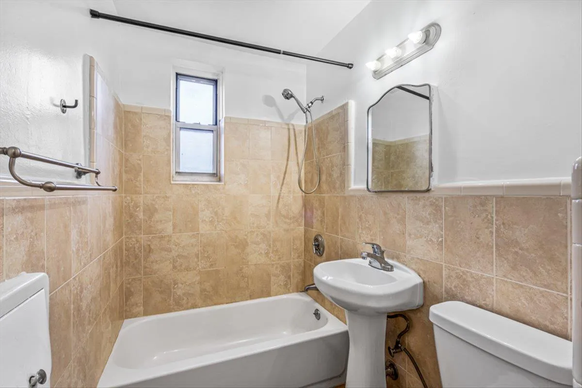 Bathroom featuring tiled shower / bath combo, tile walls, and toilet Bathroom featuring tiled shower / bath combo, tile walls, and toilet