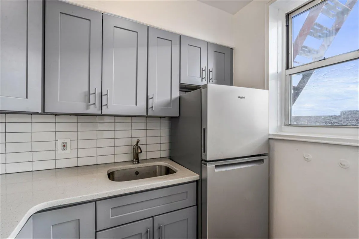 Kitchen featuring sink, gray cabinetry, stainless steel refrigerator, light stone countertops, and backsplash Kitchen featuring sink, gray cabinetry, stainless steel refrigerator, light stone countertops, and backsplash
