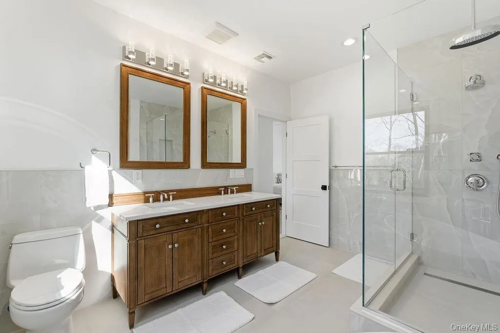 Full bathroom featuring double vanity, a marble finish shower, tile walls, and light floors Full bathroom featuring double vanity, a marble finish shower, tile walls, and light floors