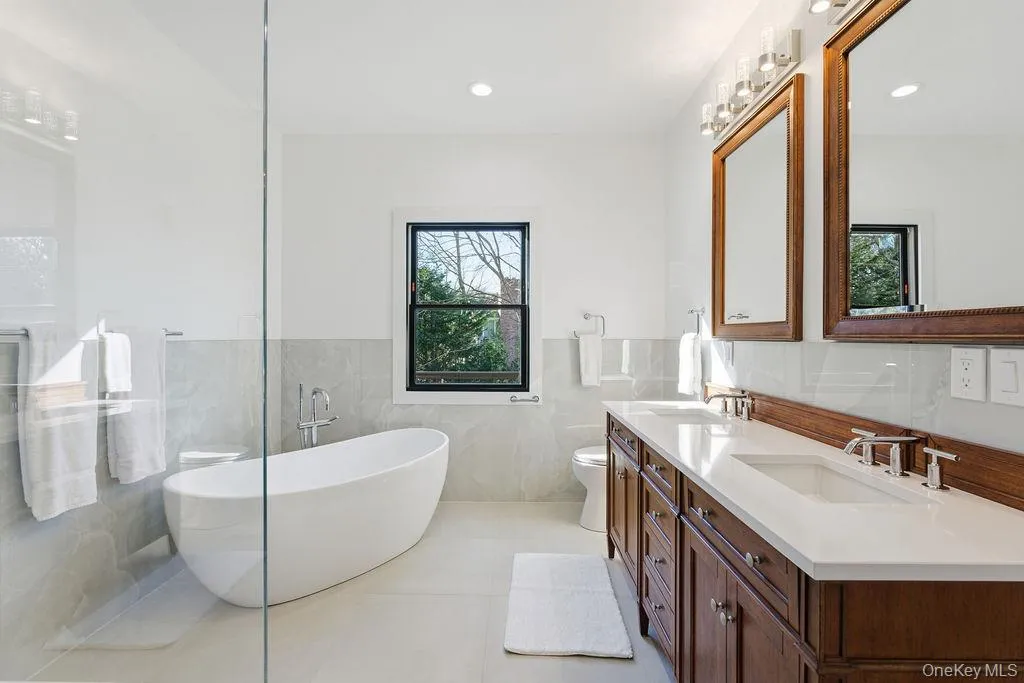 Bathroom with a freestanding tub, double vanity, light tile patterned floors, a wainscoted wall, and tile walls Bathroom with a freestanding tub, double vanity, light tile patterned floors, a wainscoted wall, and tile walls