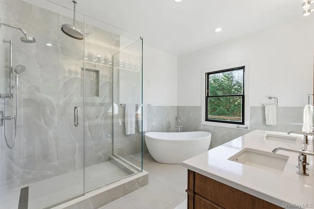 Full bathroom with a freestanding tub, double vanity, tile walls, a marble finish shower, and wainscoting Full bathroom with a freestanding tub, double vanity, tile walls, a marble finish shower, and wainscoting