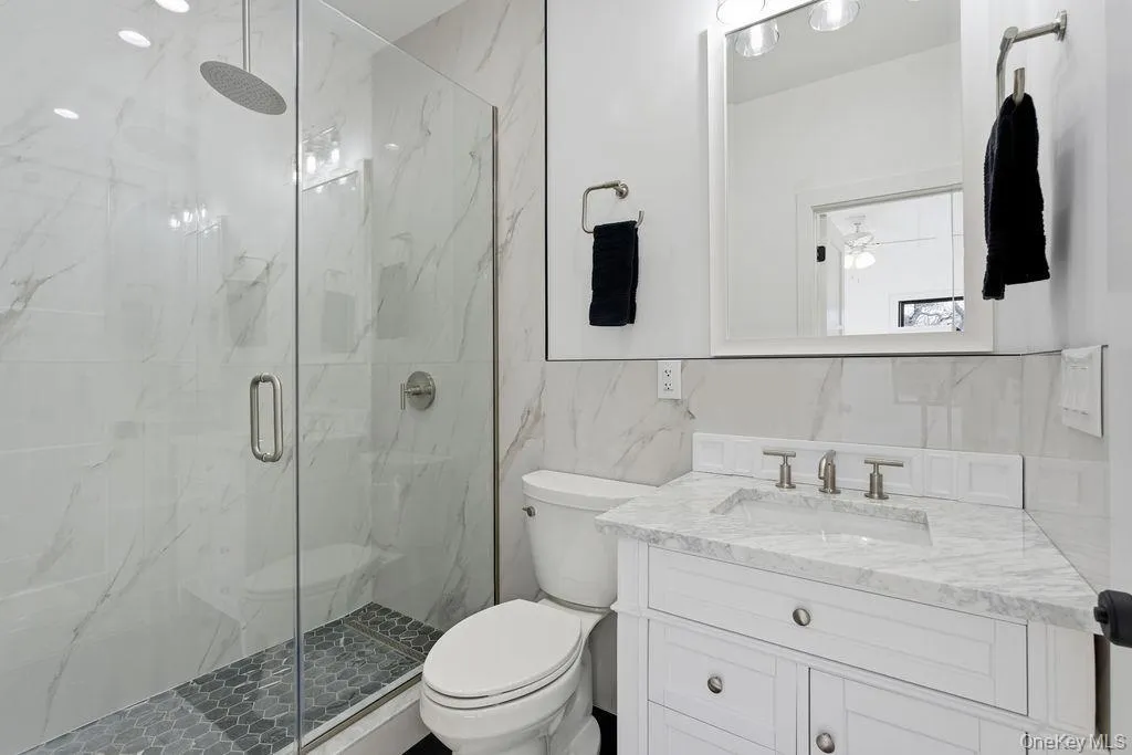 Bathroom with tile walls, vanity, a marble finish shower, tasteful backsplash, and ceiling fan Bathroom with tile walls, vanity, a marble finish shower, tasteful backsplash, and ceiling fan