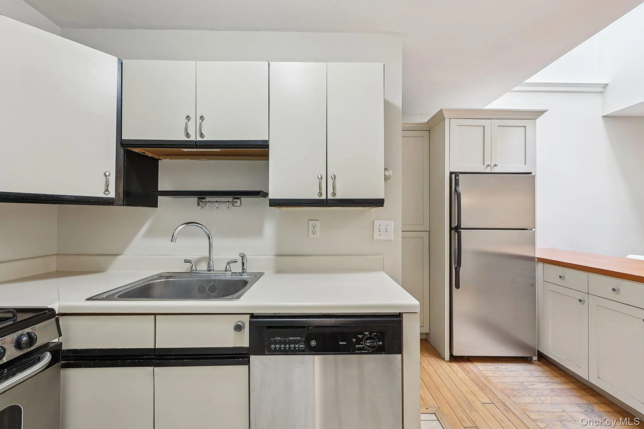 Kitchen featuring light wood-type flooring, light countertops, white cabinets, a sink, and appliances with stainless steel finishes Kitchen featuring light wood-type flooring, light countertops, white cabinets, a sink, and appliances with stainless steel finishes