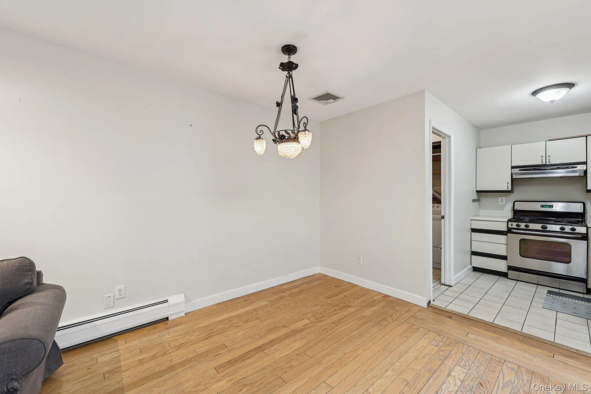 Kitchen featuring stainless steel gas stove, baseboard heating, under cabinet range hood, white cabinets, and light wood finished floors Kitchen featuring stainless steel gas stove, baseboard heating, under cabinet range hood, white cabinets, and light wood finished floors