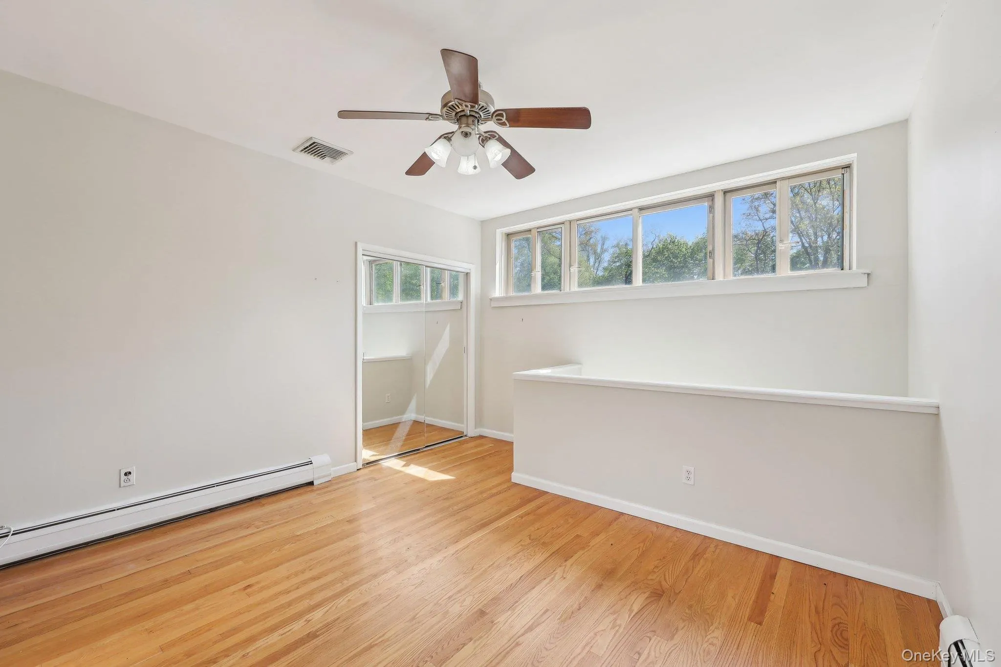 Empty room featuring baseboards, a baseboard radiator, wood finished floors, and visible vents Empty room featuring baseboards, a baseboard radiator, wood finished floors, and visible vents