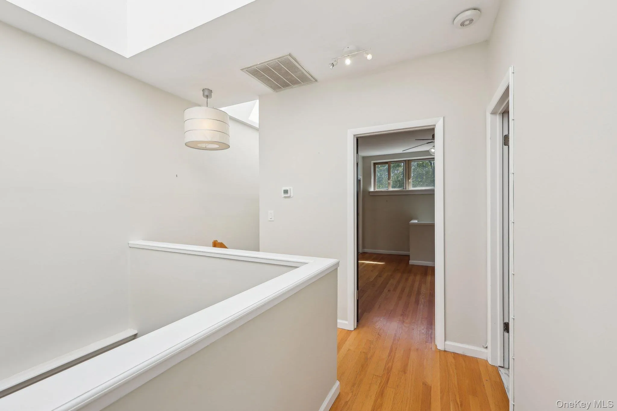 Hallway featuring a skylight, light wood-style floors, an upstairs landing, and visible vents Hallway featuring a skylight, light wood-style floors, an upstairs landing, and visible vents