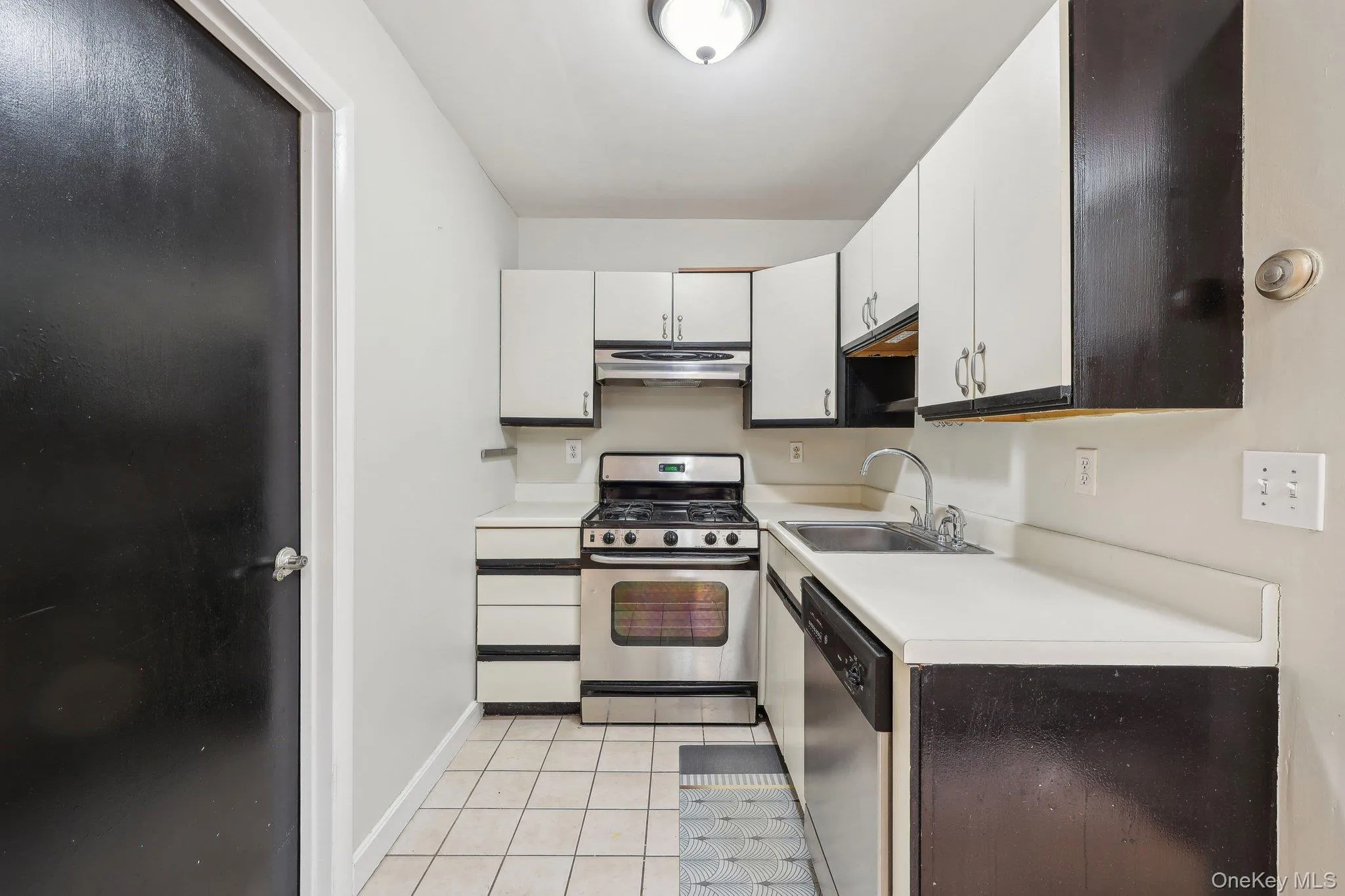 Kitchen with appliances with stainless steel finishes, a sink, light countertops, white cabinetry, and under cabinet range hood Kitchen with appliances with stainless steel finishes, a sink, light countertops, white cabinetry, and under cabinet range hood