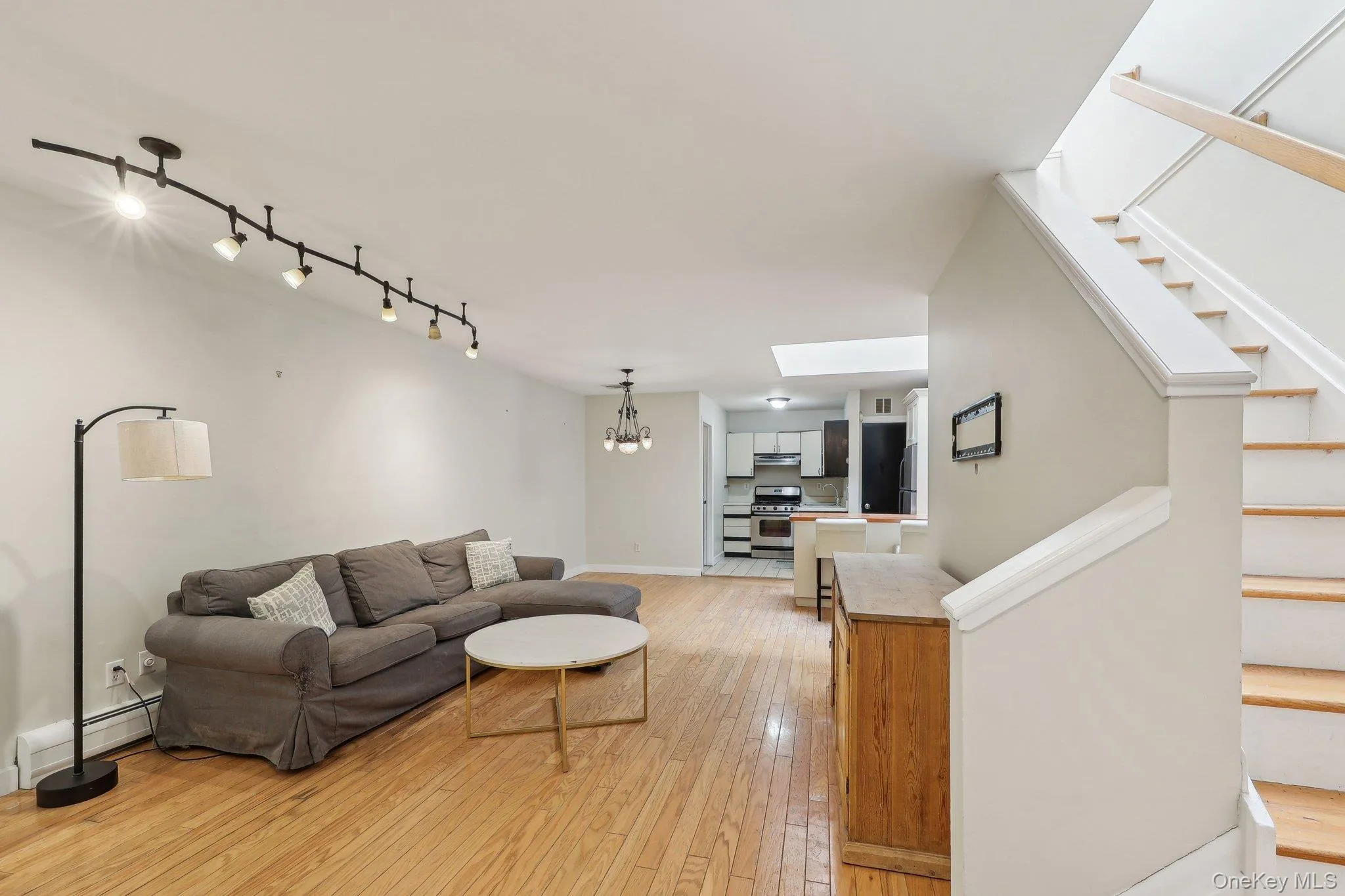 Living room with track lighting, baseboards, stairway, light wood-type flooring, and a chandelier Living room with track lighting, baseboards, stairway, light wood-type flooring, and a chandelier