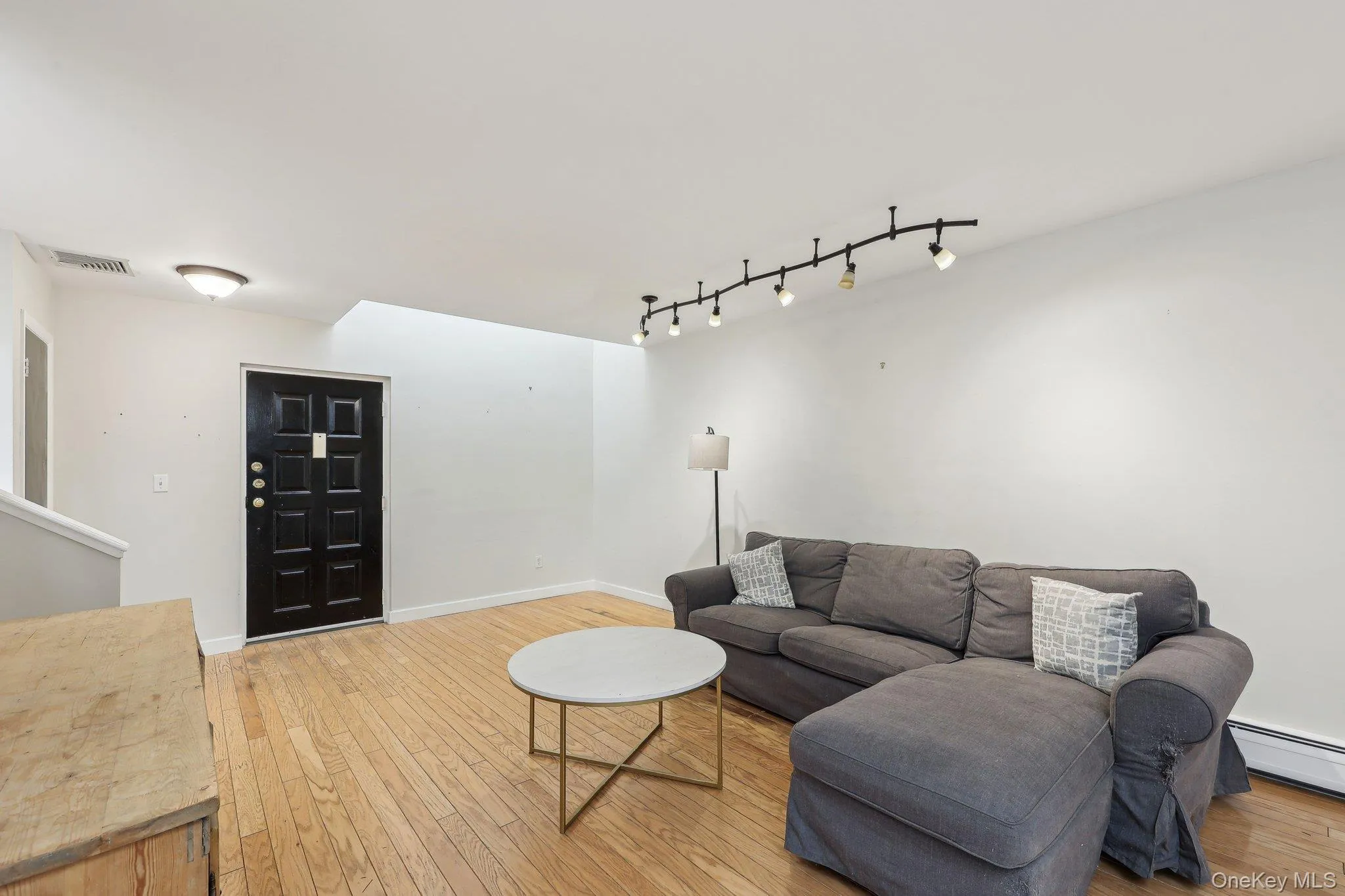 Living room featuring visible vents, track lighting, baseboards, baseboard heating, and light wood finished floors Living room featuring visible vents, track lighting, baseboards, baseboard heating, and light wood finished floors