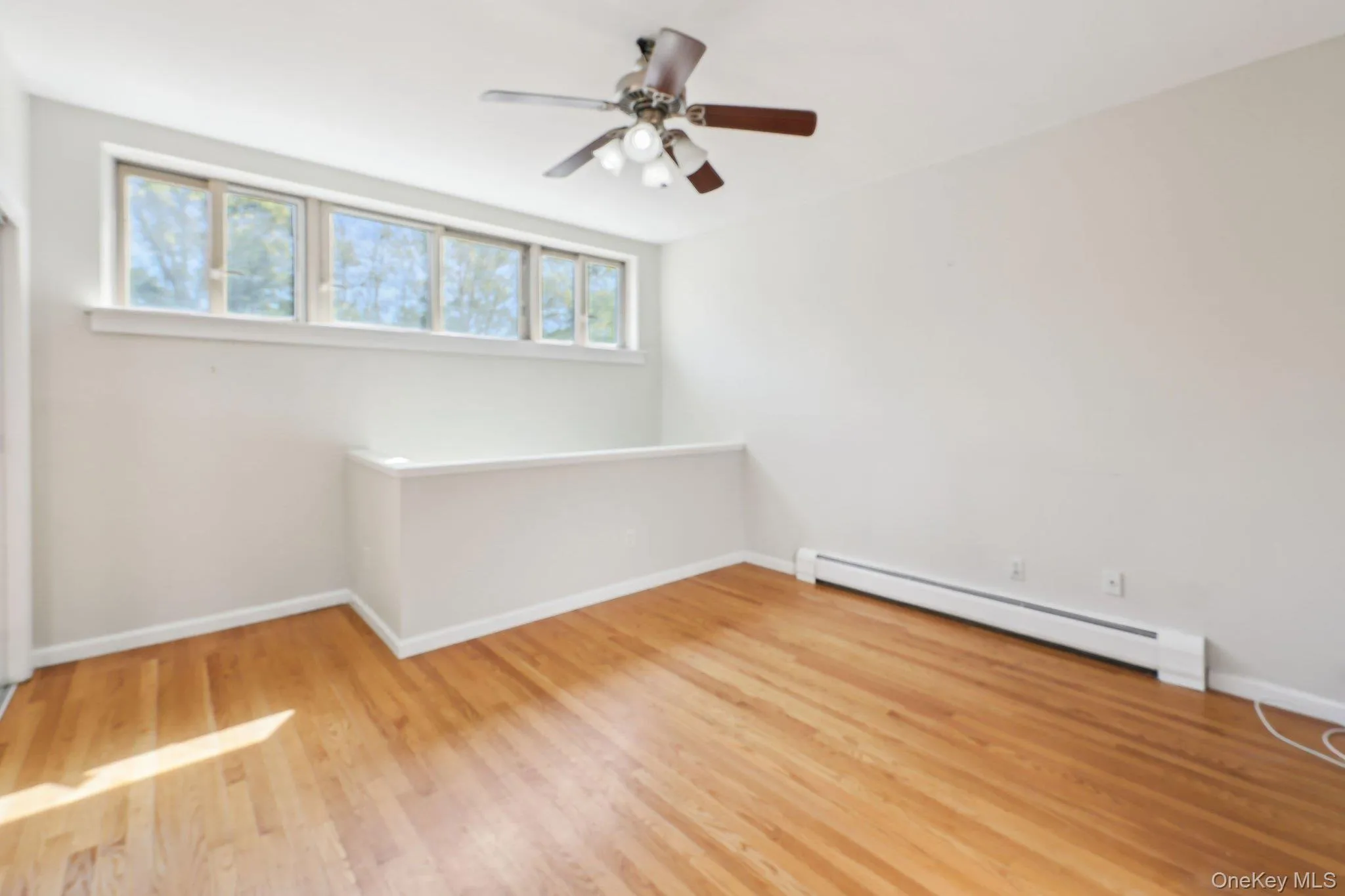 Empty room with plenty of natural light, a ceiling fan, a baseboard heating unit, and wood finished floors Empty room with plenty of natural light, a ceiling fan, a baseboard heating unit, and wood finished floors