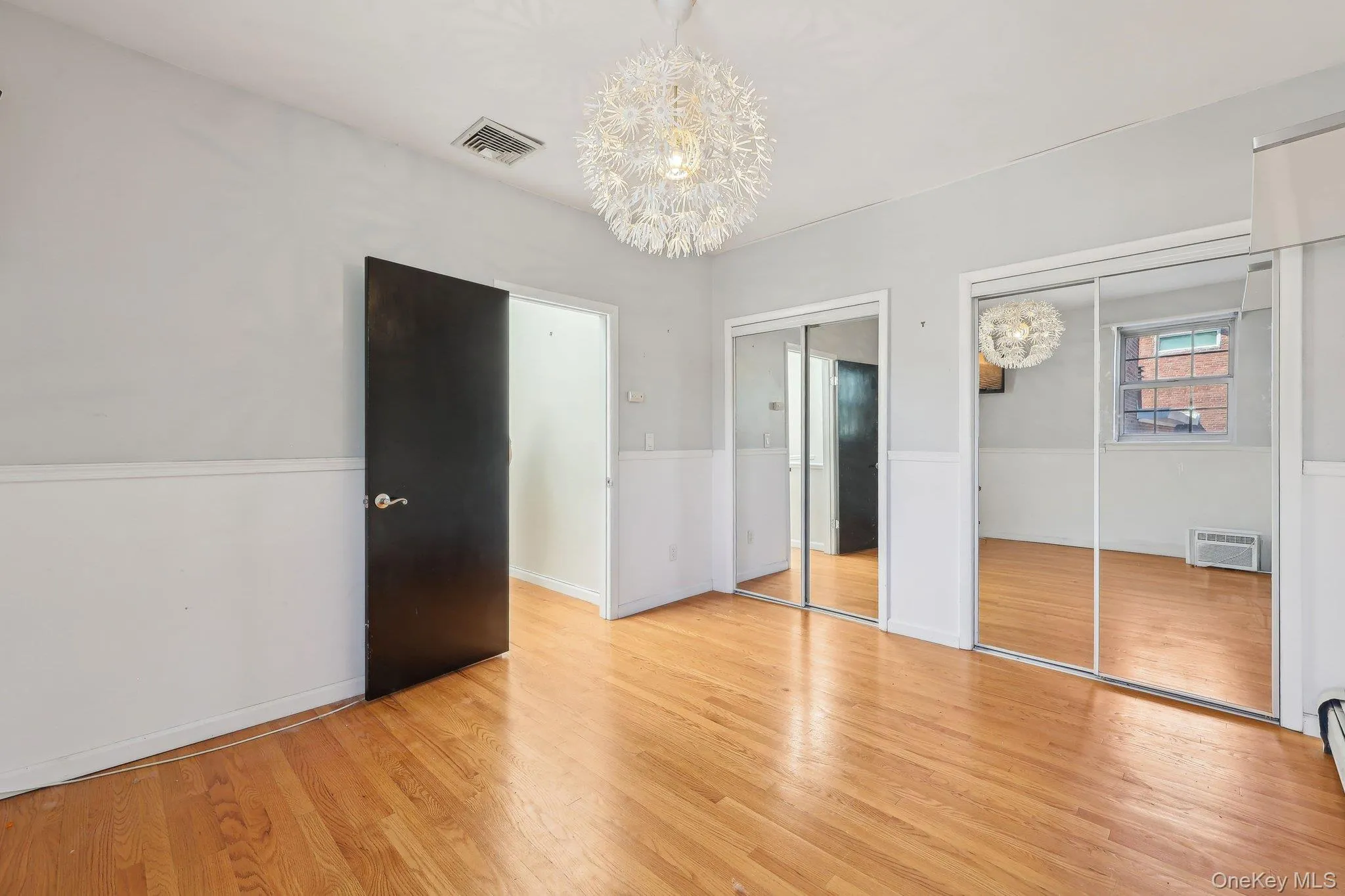 Unfurnished bedroom featuring visible vents, multiple closets, a notable chandelier, and light wood finished floors Unfurnished bedroom featuring visible vents, multiple closets, a notable chandelier, and light wood finished floors
