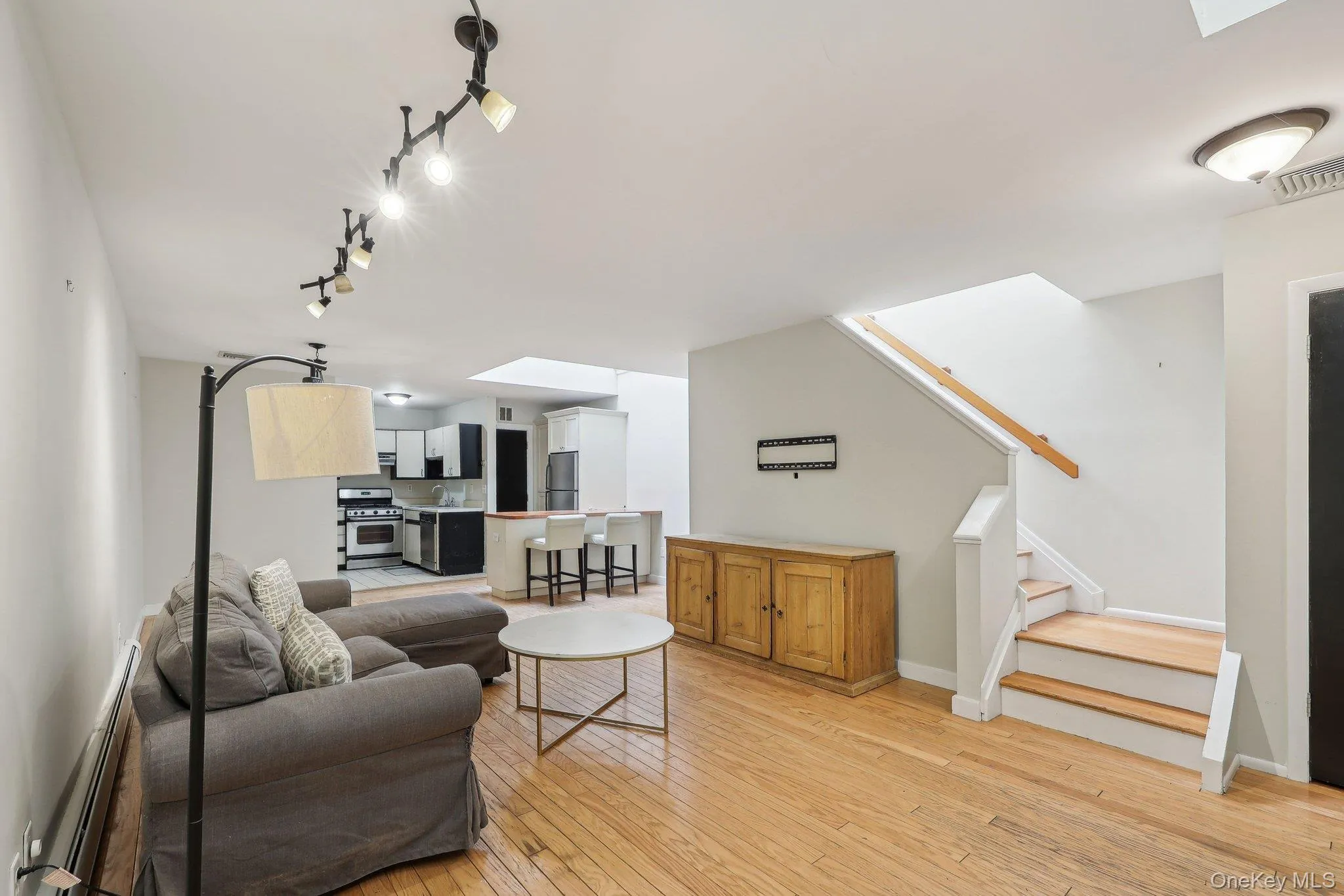Living area with track lighting, light wood-style flooring, stairs, and a skylight Living area with track lighting, light wood-style flooring, stairs, and a skylight