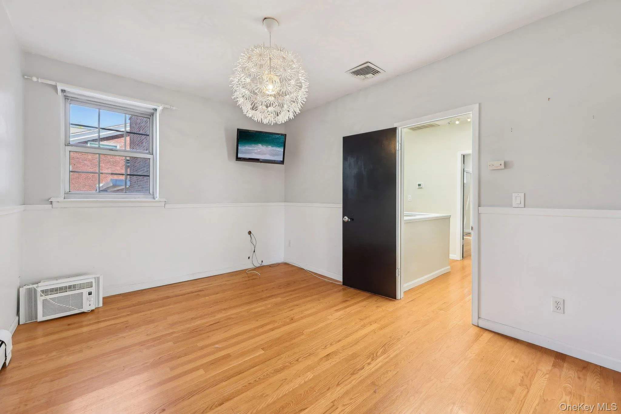 Empty room with visible vents, light wood-type flooring, a wall mounted AC, a baseboard radiator, and a notable chandelier Empty room with visible vents, light wood-type flooring, a wall mounted AC, a baseboard radiator, and a notable chandelier