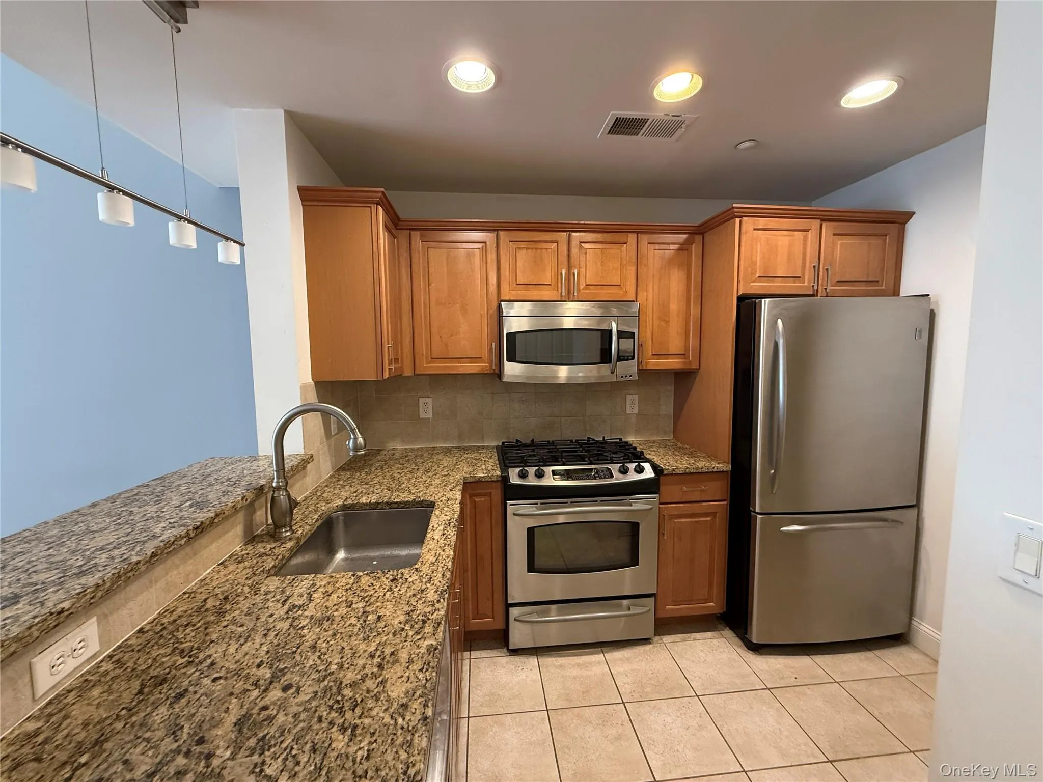 Kitchen with a sink, dark stone counters, stainless steel appliances, decorative backsplash, and visible vents Kitchen with a sink, dark stone counters, stainless steel appliances, decorative backsplash, and visible vents
