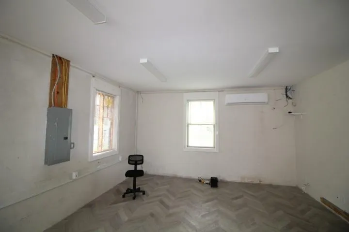 Empty room featuring an AC wall unit, plenty of natural light, and electric panel Empty room featuring an AC wall unit, plenty of natural light, and electric panel