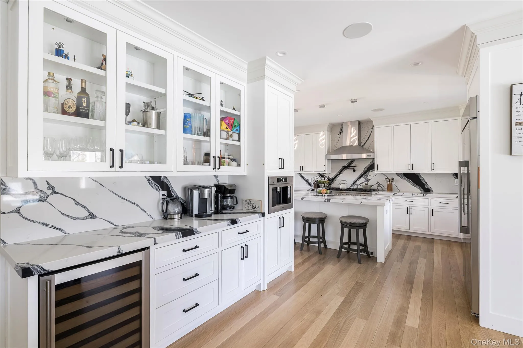 Bar with wall chimney range hood, appliances with stainless steel finishes, light wood finished floors, wine cooler, and pendant lighting Bar with wall chimney range hood, appliances with stainless steel finishes, light wood finished floors, wine cooler, and pendant lighting