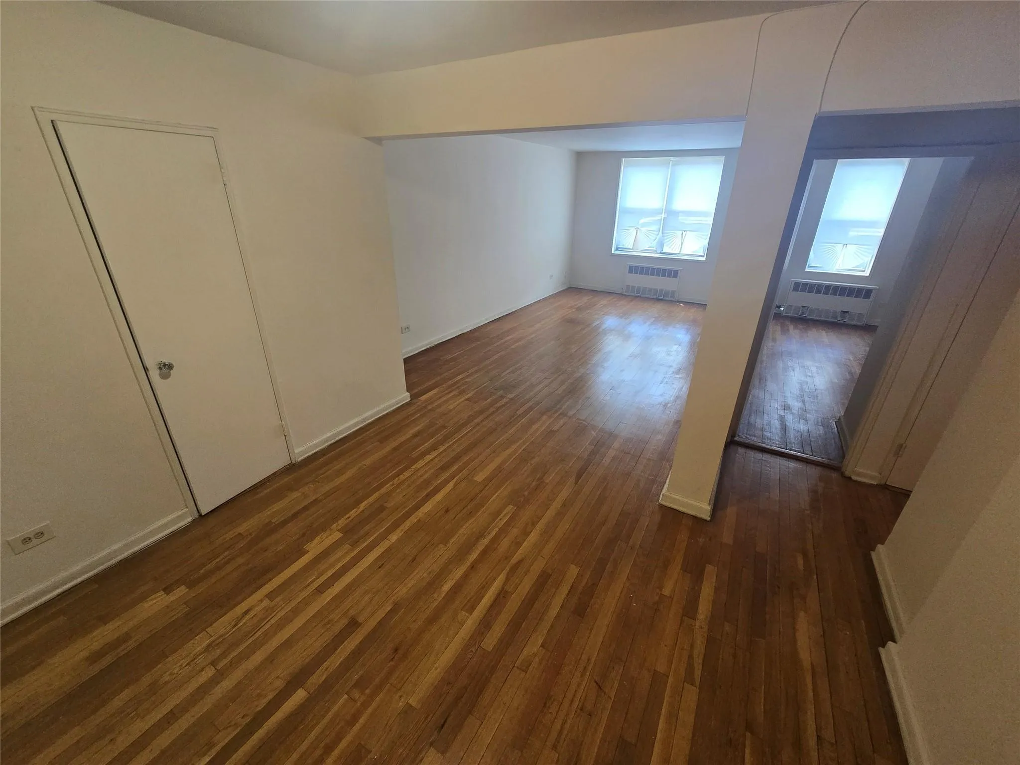 Unfurnished bedroom featuring radiator heating unit and dark wood-style floors Unfurnished bedroom featuring radiator heating unit and dark wood-style floors