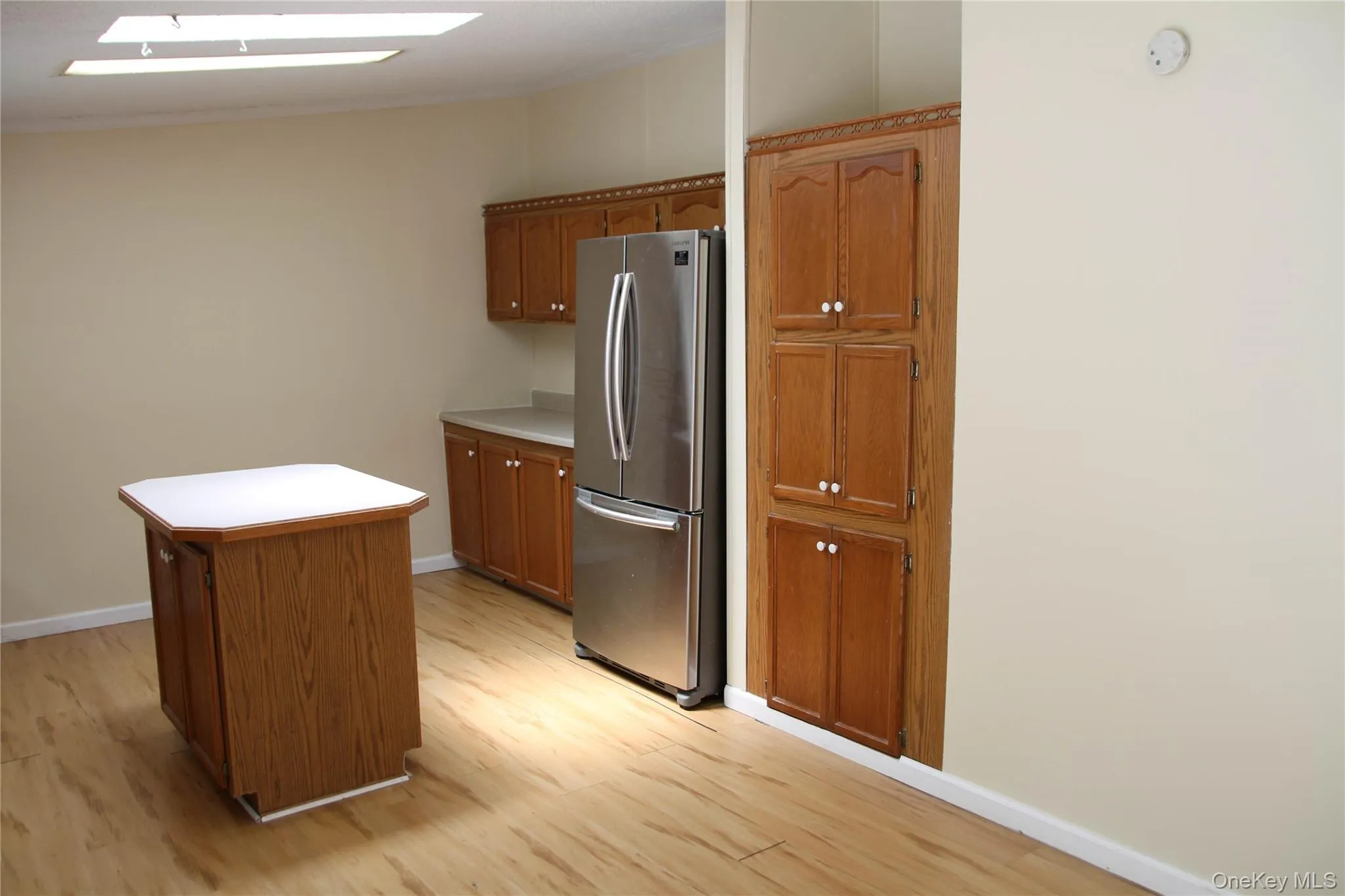 Kitchen with freestanding refrigerator, light wood finished floors, brown cabinets, and ornamental molding Kitchen with freestanding refrigerator, light wood finished floors, brown cabinets, and ornamental molding