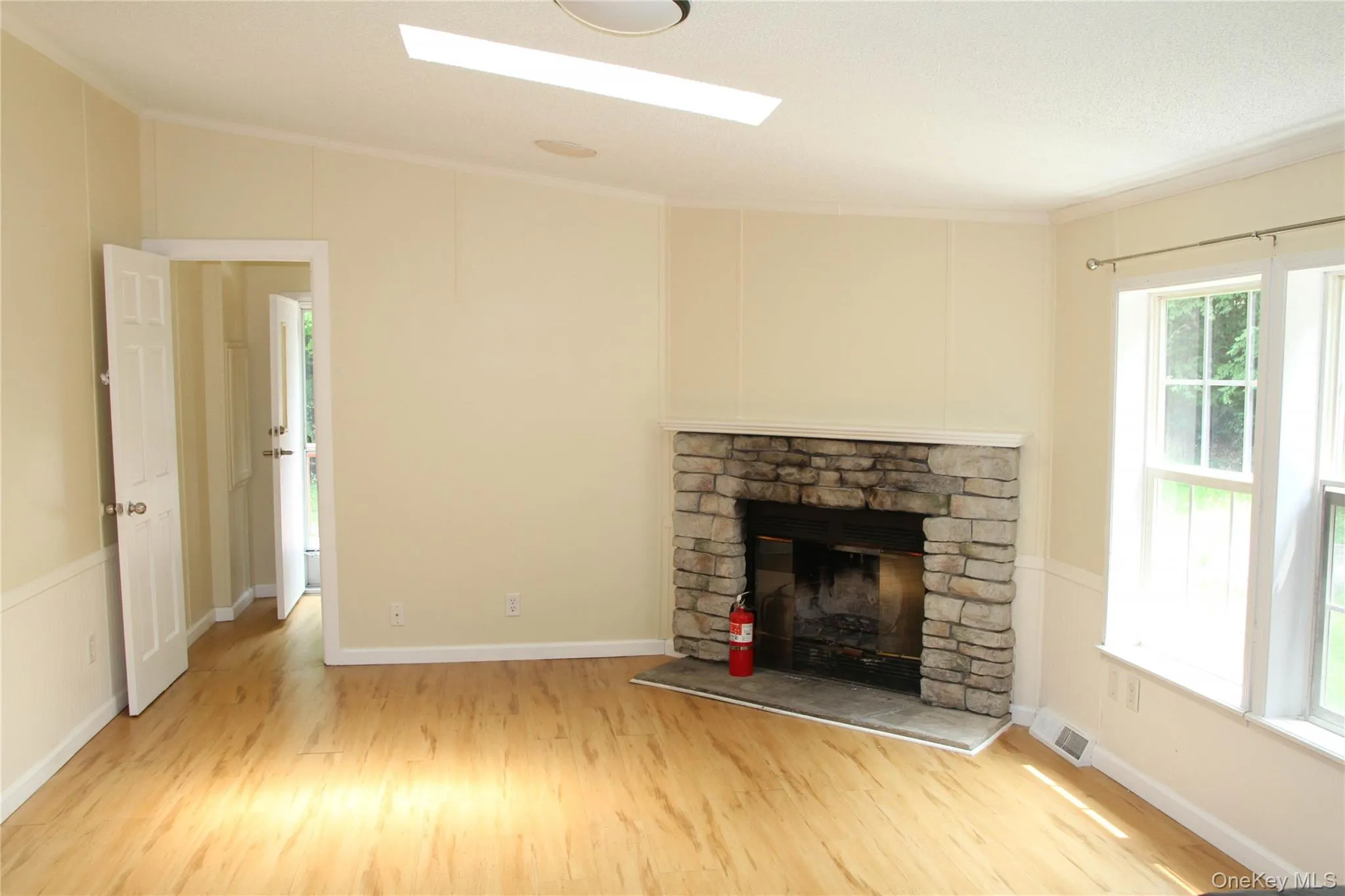 Unfurnished living room featuring wood finished floors, a stone fireplace, and ornamental molding Unfurnished living room featuring wood finished floors, a stone fireplace, and ornamental molding
