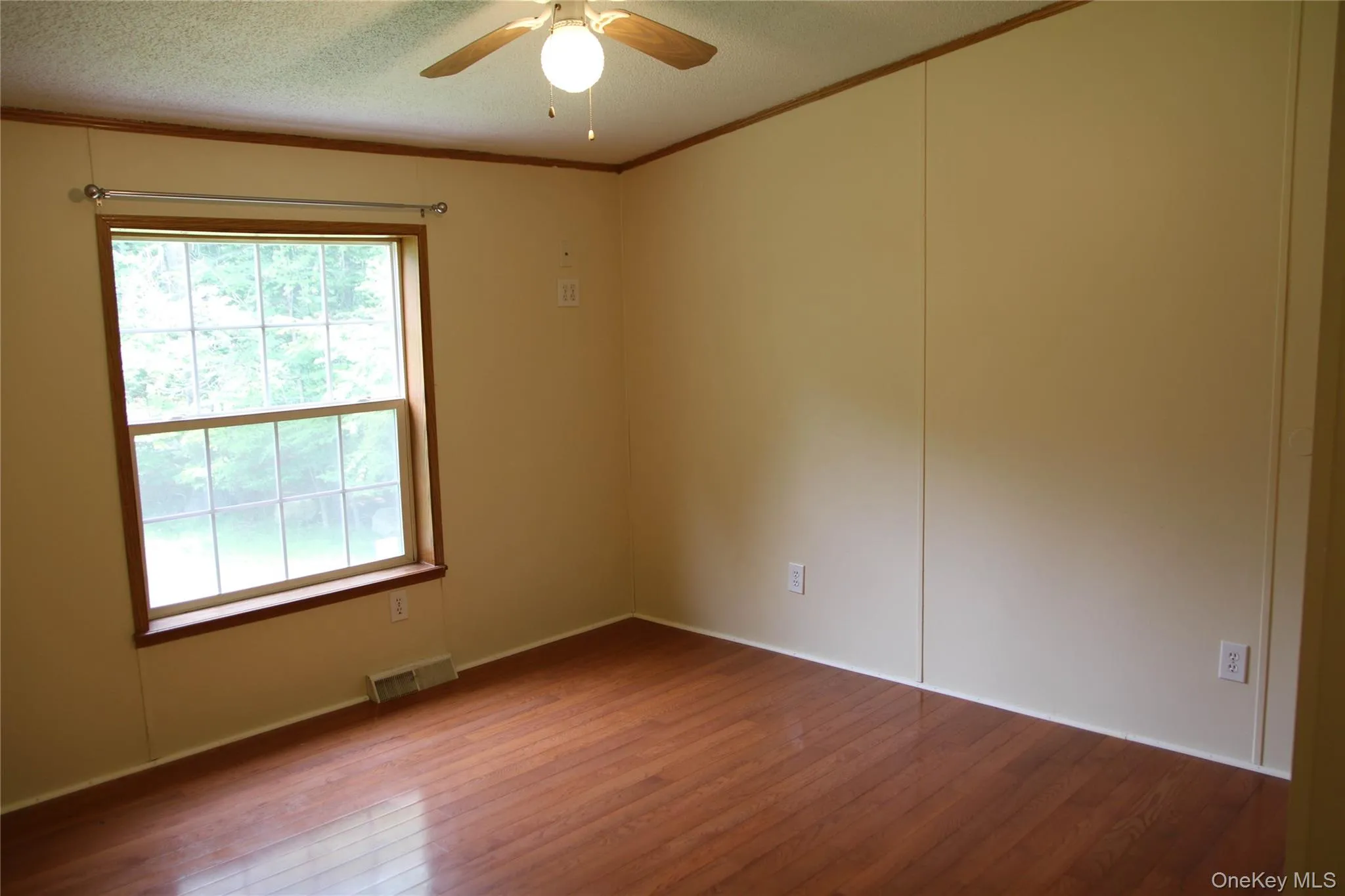 Unfurnished room featuring wood finished floors, healthy amount of natural light, ceiling fan, ornamental molding, and a textured ceiling Unfurnished room featuring wood finished floors, healthy amount of natural light, ceiling fan, ornamental molding, and a textured ceiling