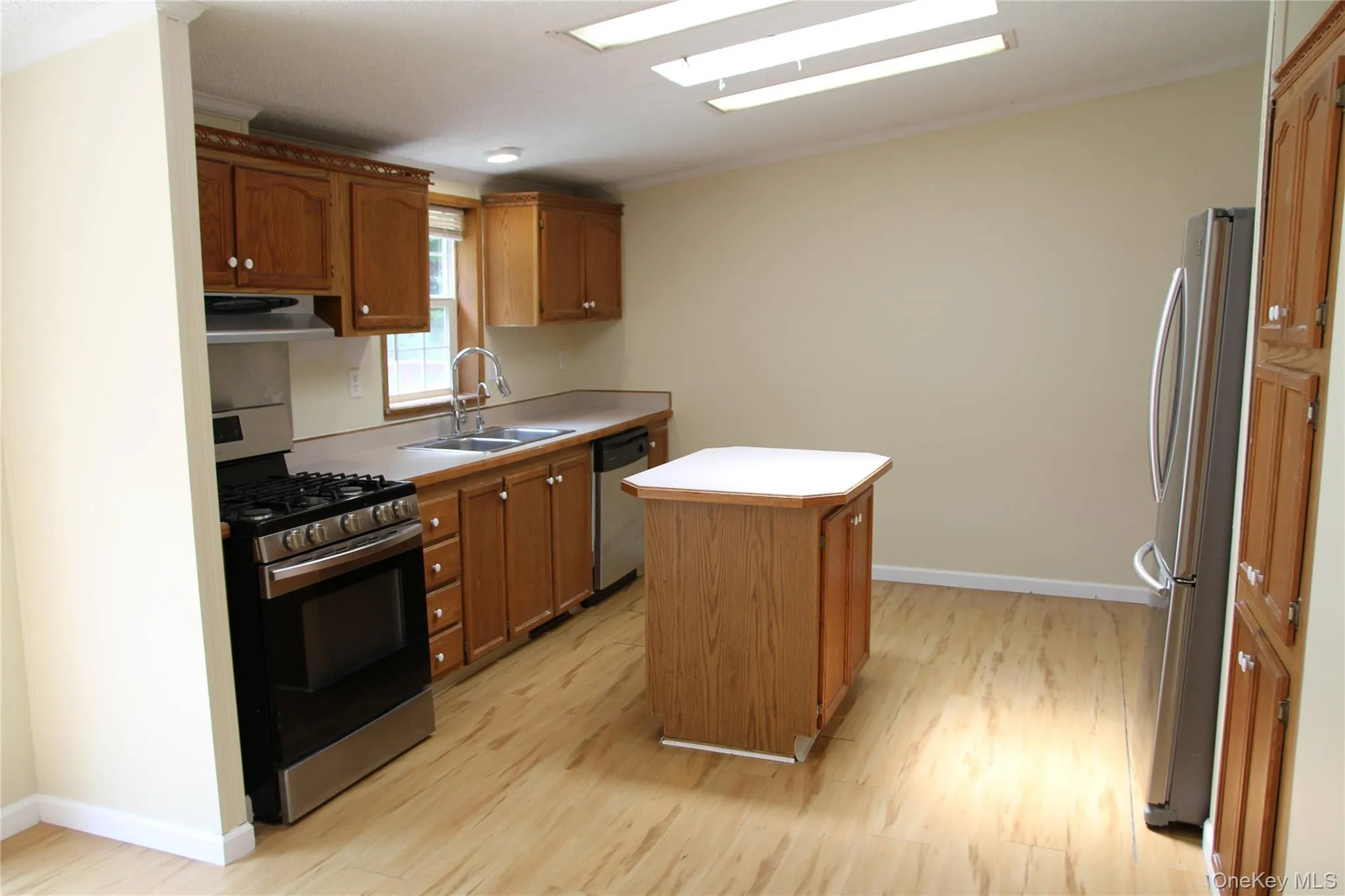 Kitchen with stainless steel appliances, ventilation hood, light wood finished floors, a kitchen island, and crown molding Kitchen with stainless steel appliances, ventilation hood, light wood finished floors, a kitchen island, and crown molding