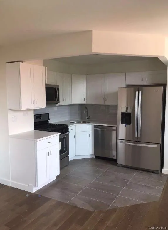 Kitchen with appliances with stainless steel finishes, tasteful backsplash, a sink, light countertops, and dark wood-style floors Kitchen with appliances with stainless steel finishes, tasteful backsplash, a sink, light countertops, and dark wood-style floors