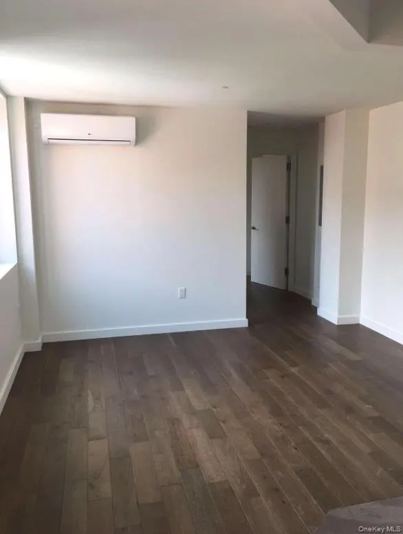 Empty room with dark wood-style flooring, baseboards, and a wall mounted air conditioner Empty room with dark wood-style flooring, baseboards, and a wall mounted air conditioner